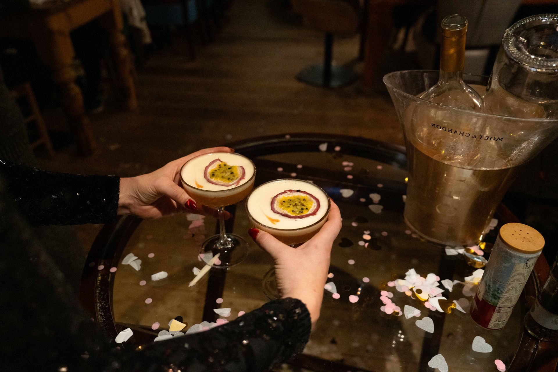 Een vrouw houdt twee cocktails in haar handen op een tafel.  bij Linke Loetje