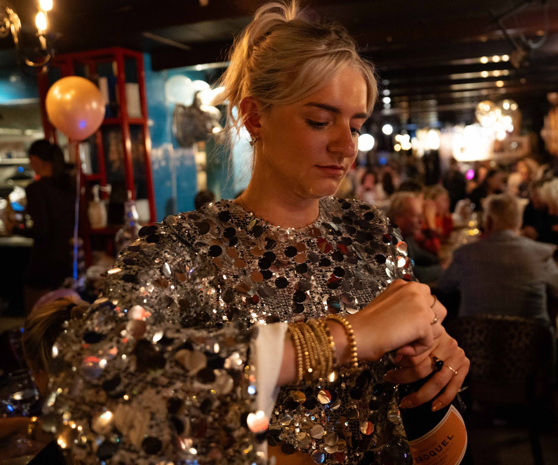 Een vrouw in een met pailletten bezette top kijkt op haar horloge