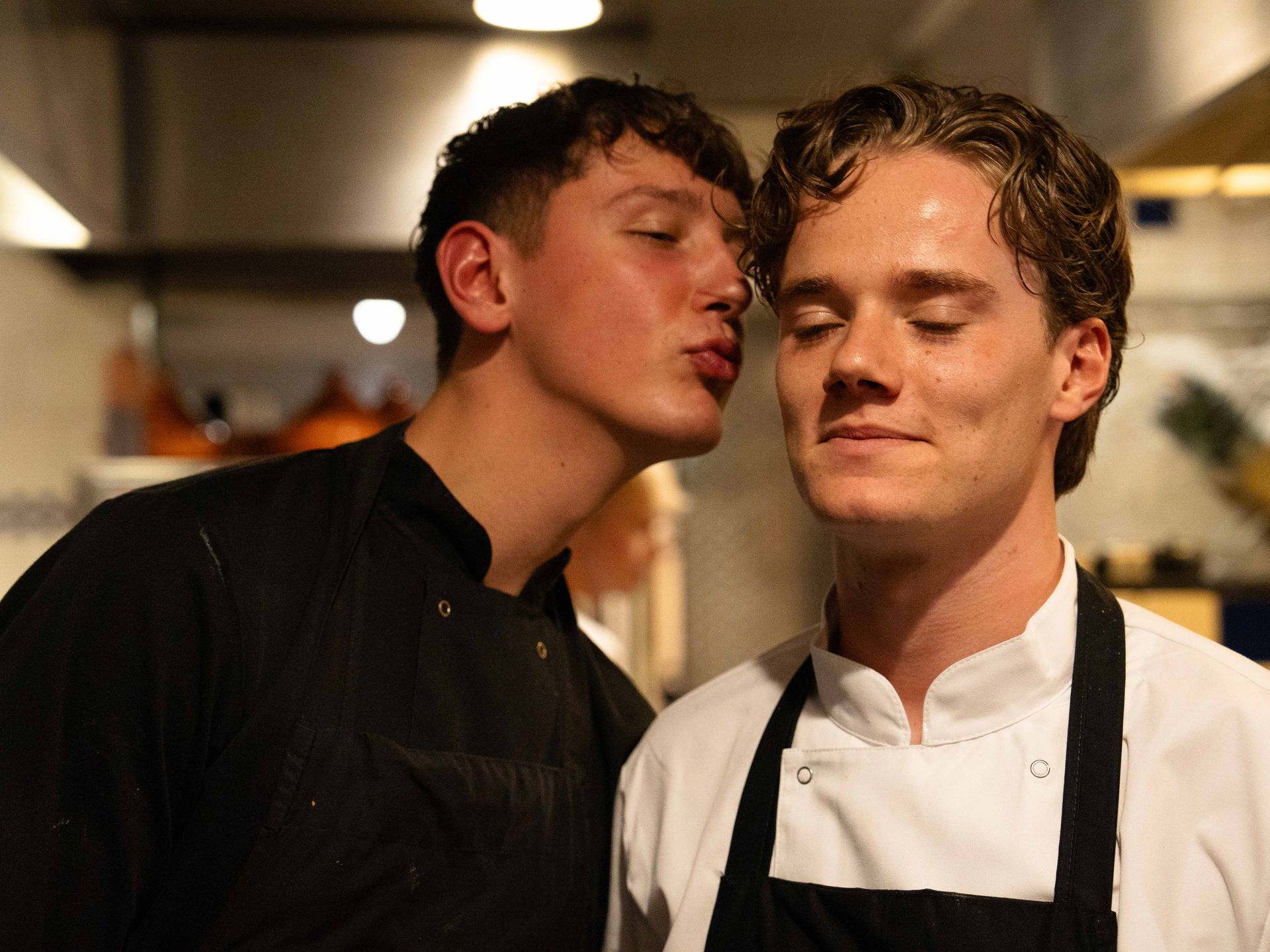 Een man kust een andere man op de wang in de keuken. . Bij Linke Loetje