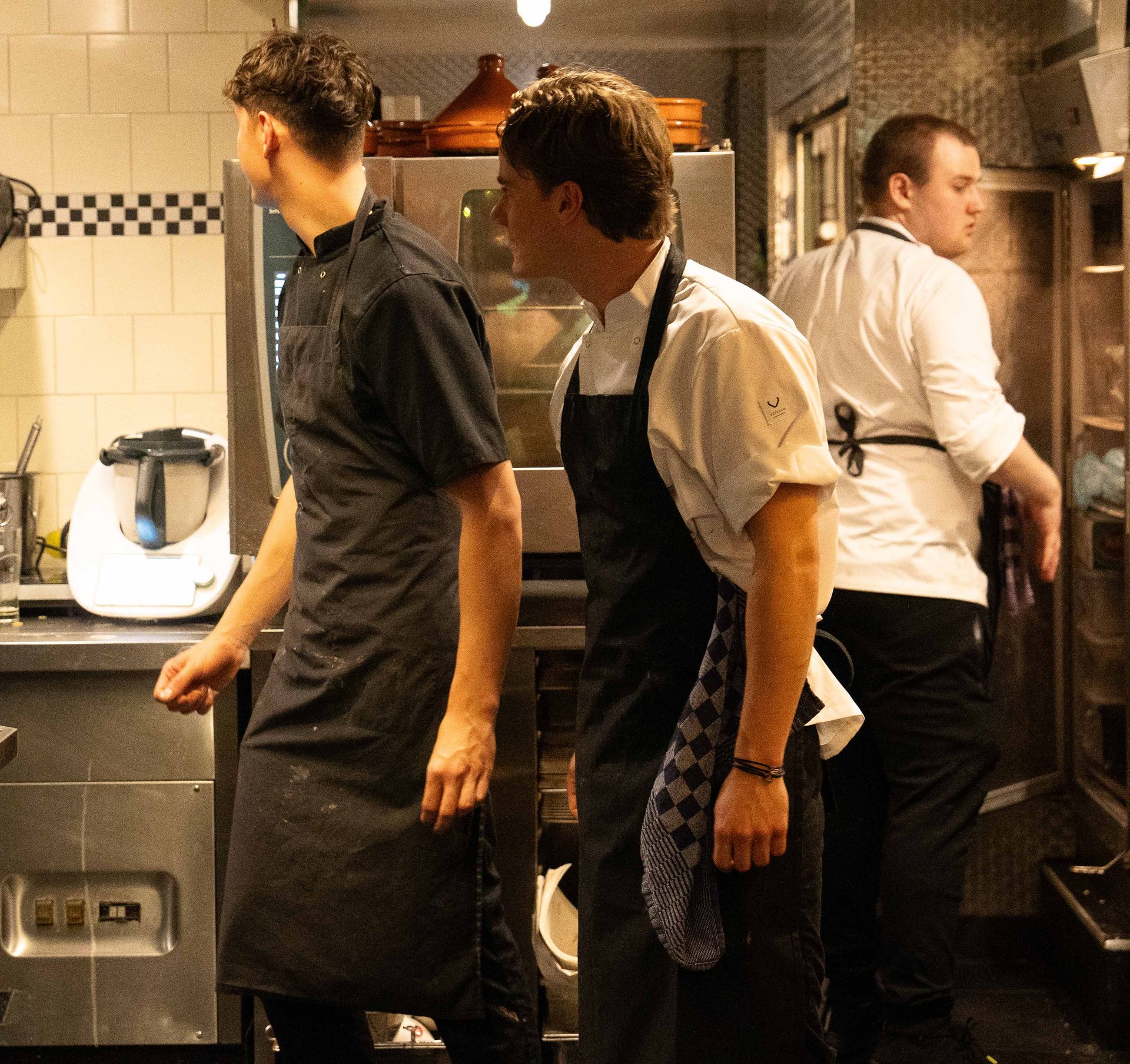 Drie mannen in schorten staan ​​in een keuken. Bij Linke Loetje