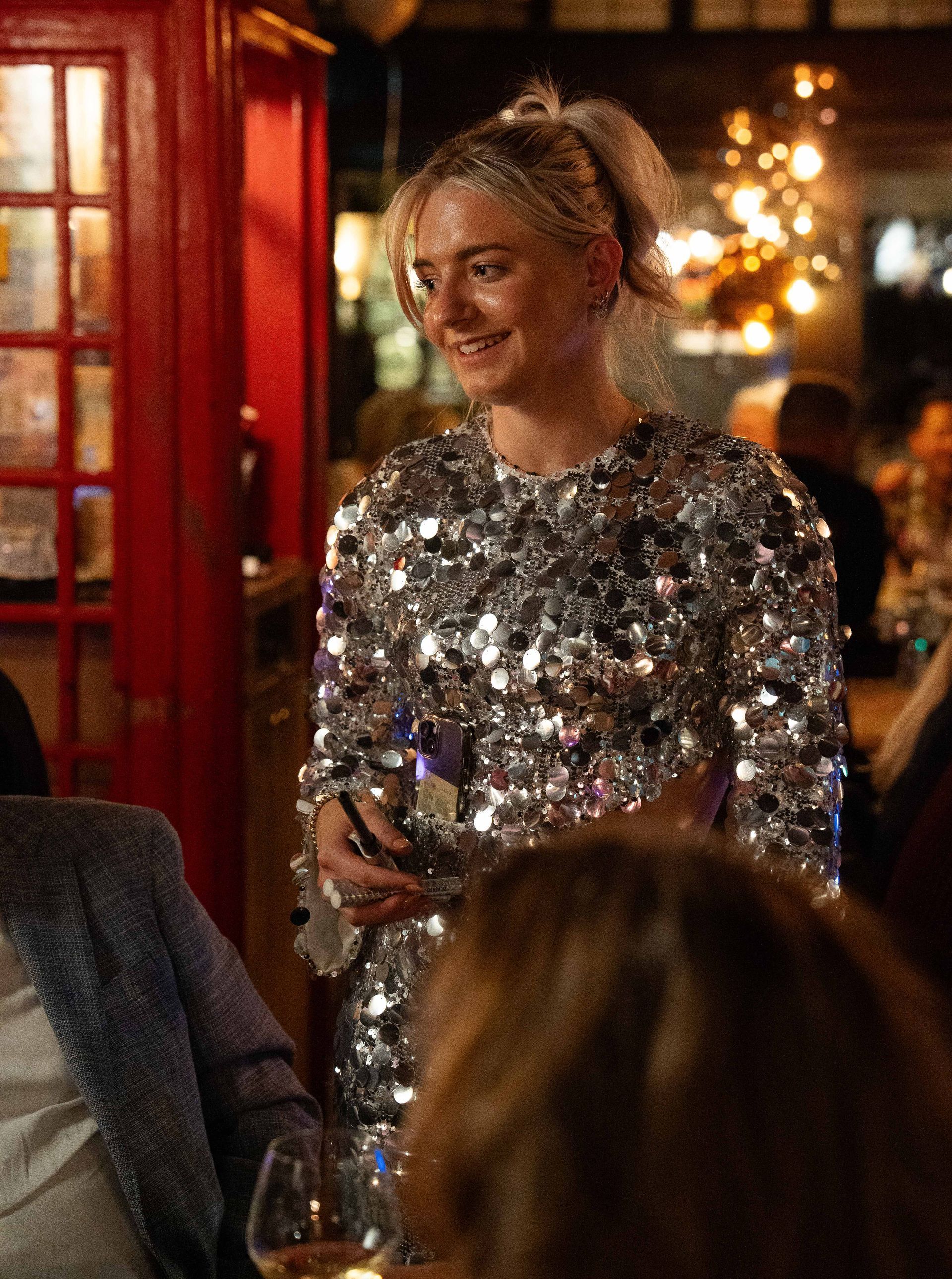 Een vrouw in een jurk met pailletten houdt een glas wijn vast in een . Bij Linke Loetjerestaurant.