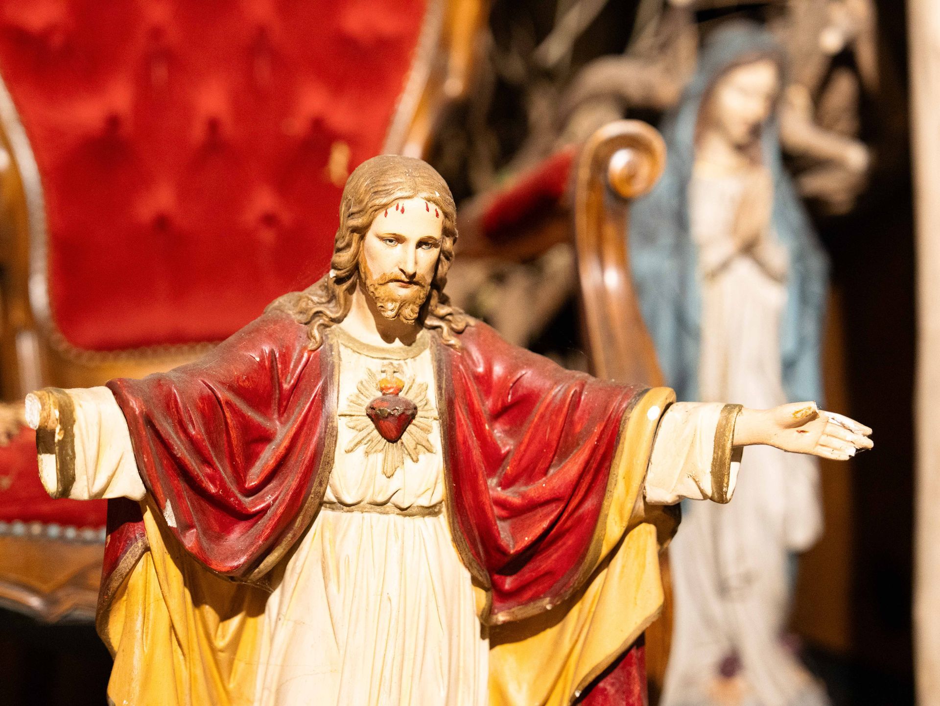 Een standbeeld van Jezus met zijn armen uitgestrekt voor een stoel.