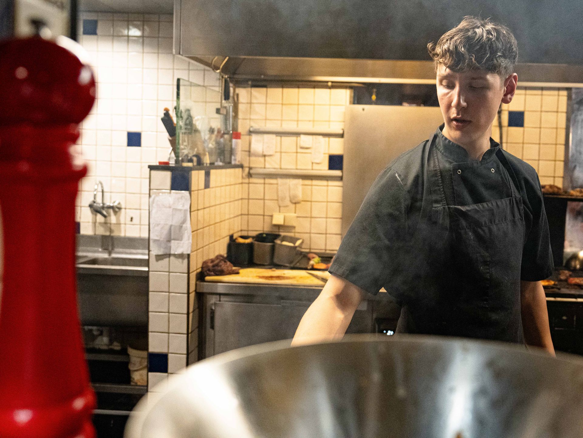 Een man met een schort voor staat in de keuken naast een grote metalen kom.