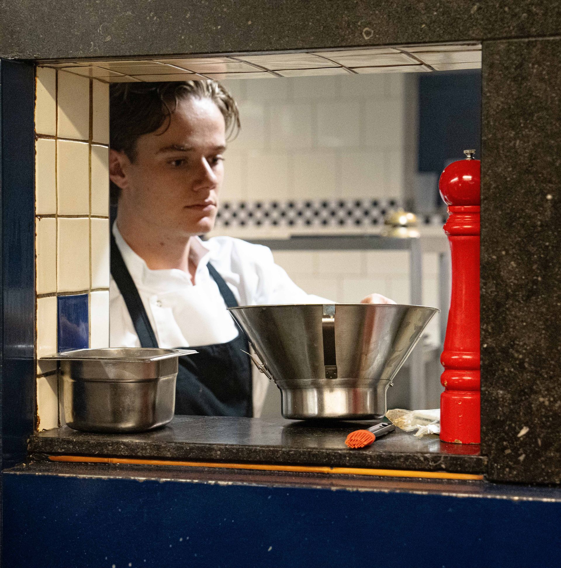 Een man met een schort kijkt door een raam naar een keuken  bij Linke Loetje