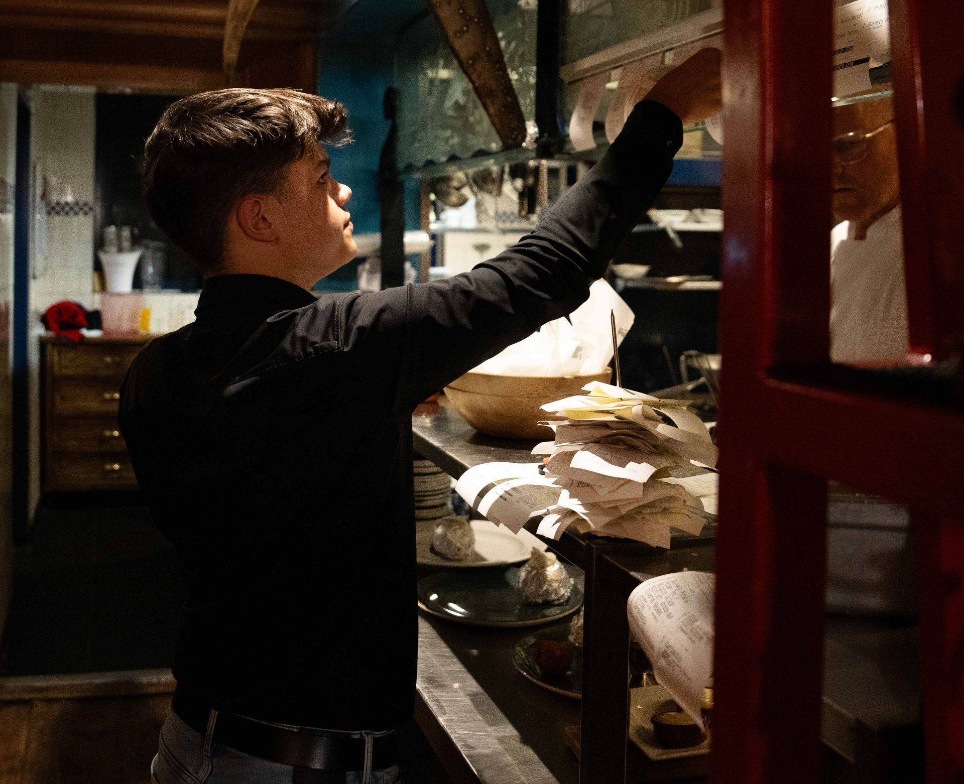 Een man in een zwart shirt grijpt naar iets in een keuken