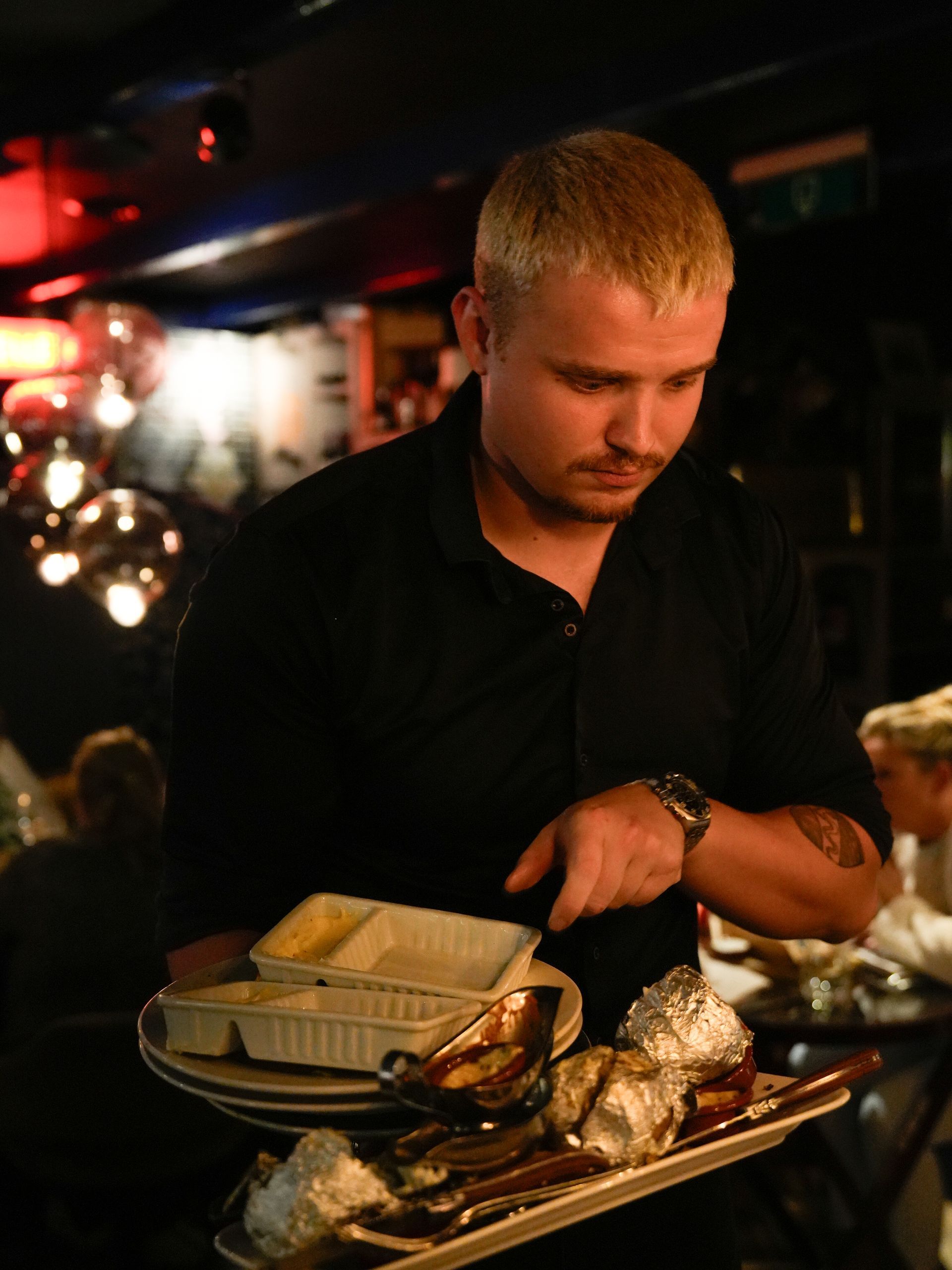 Een man in een zwart shirt houdt een dienblad met eten vast. Bij Linke Loetje