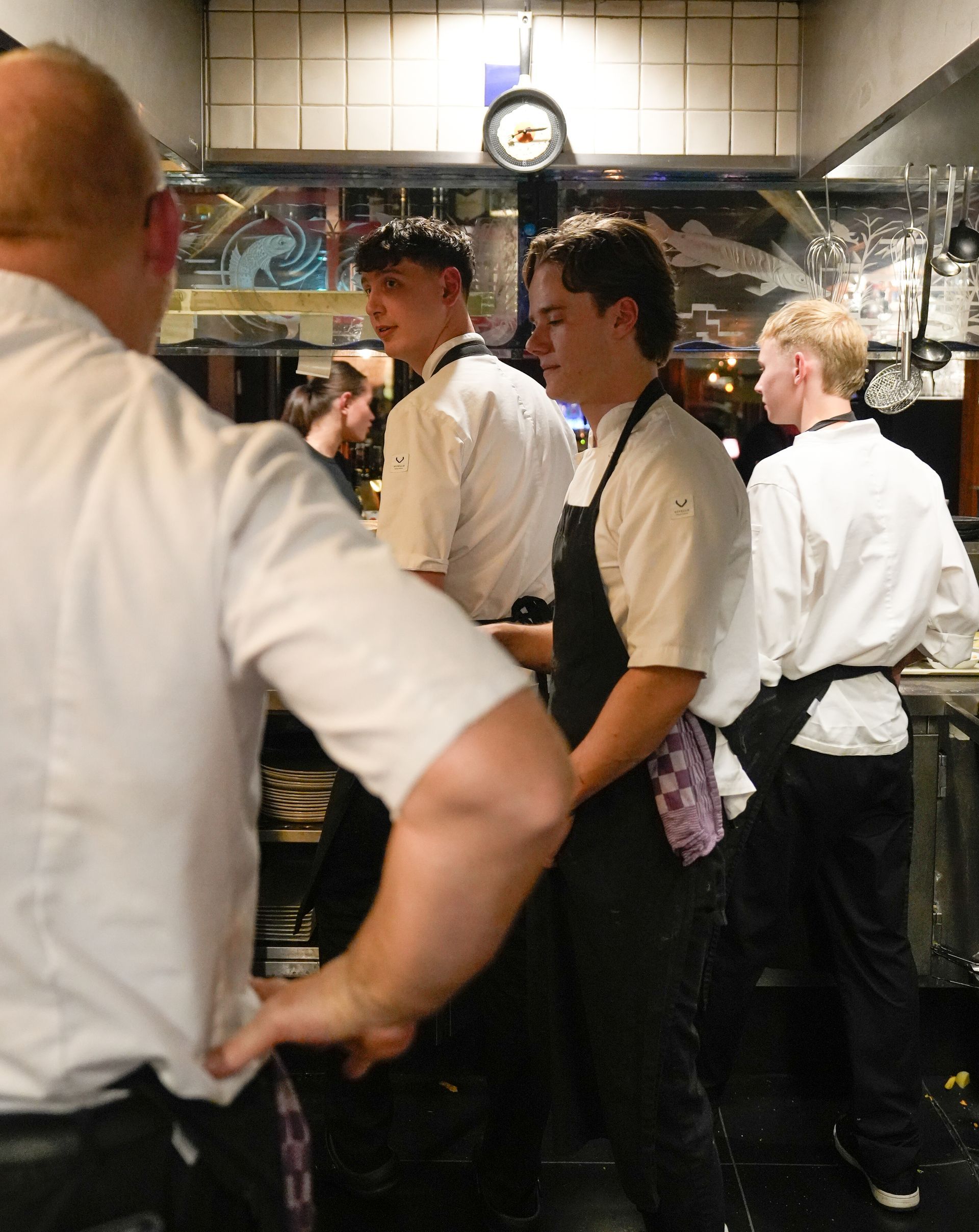 Een groep mannen staat in een keuken met een klok aan de muur. Bij Linke Loetje