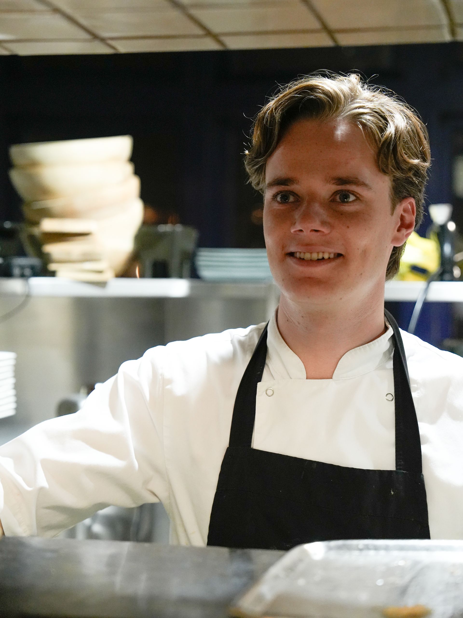 Een man in een koksuniform en schort lacht. Bij Linke Loetje