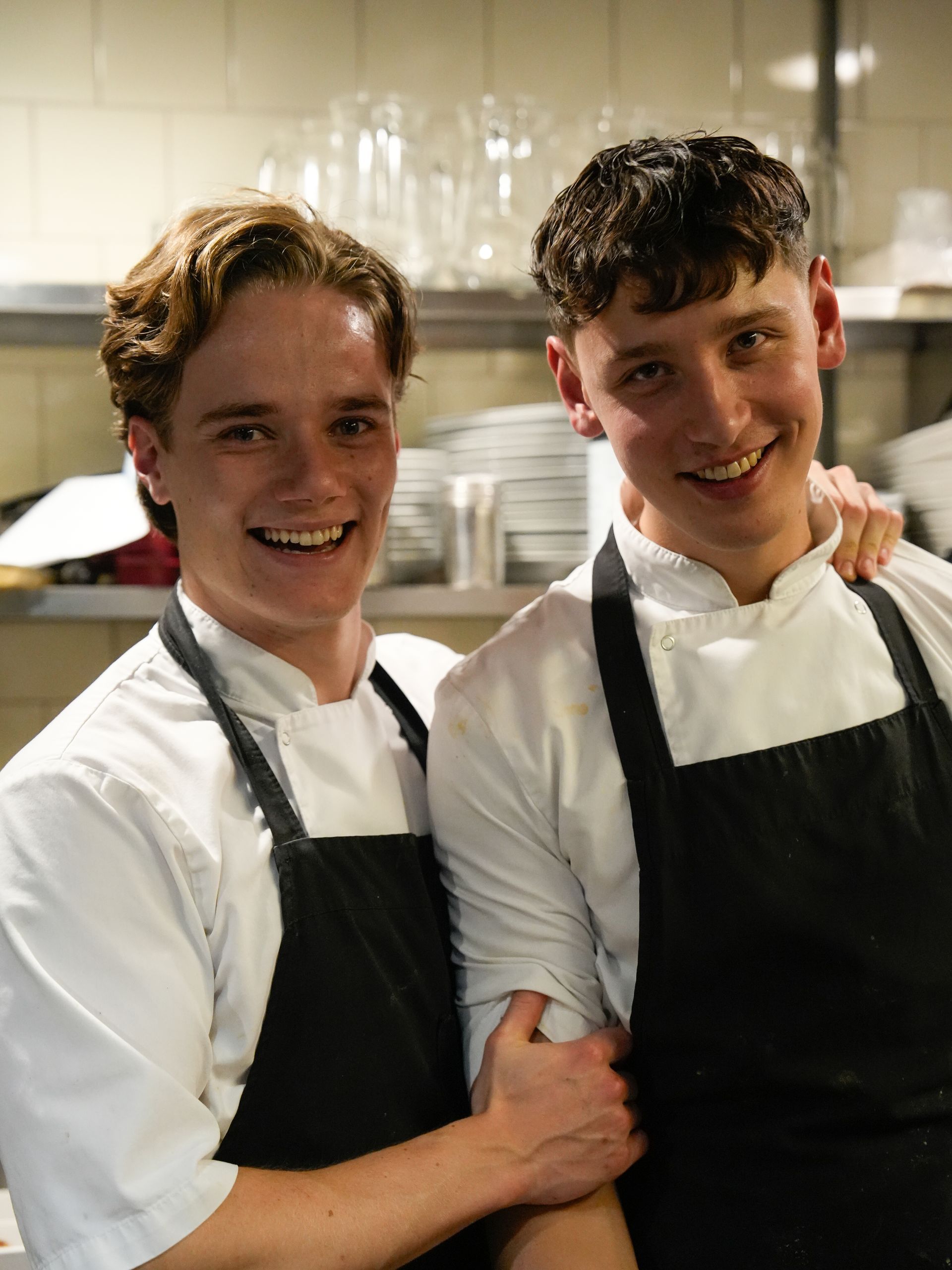 Twee jongemannen met schorten poseren voor een foto in een keuken.. Bij Linke Loetje
