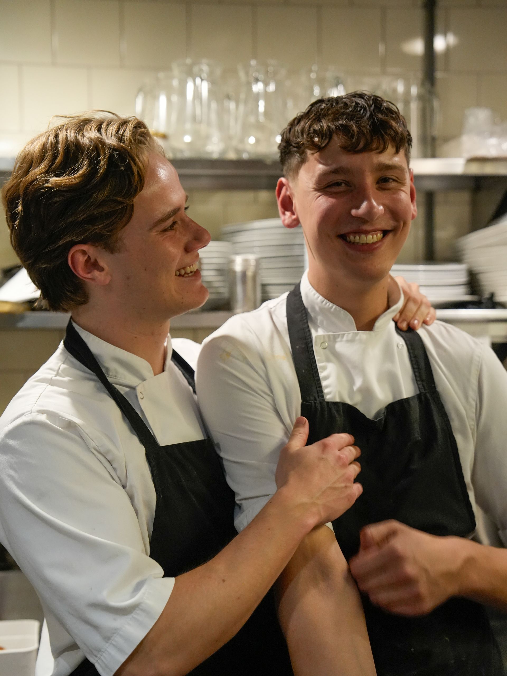 Twee mannen met schorten omhelzen elkaar in een keuken.  bij Linke Loetje