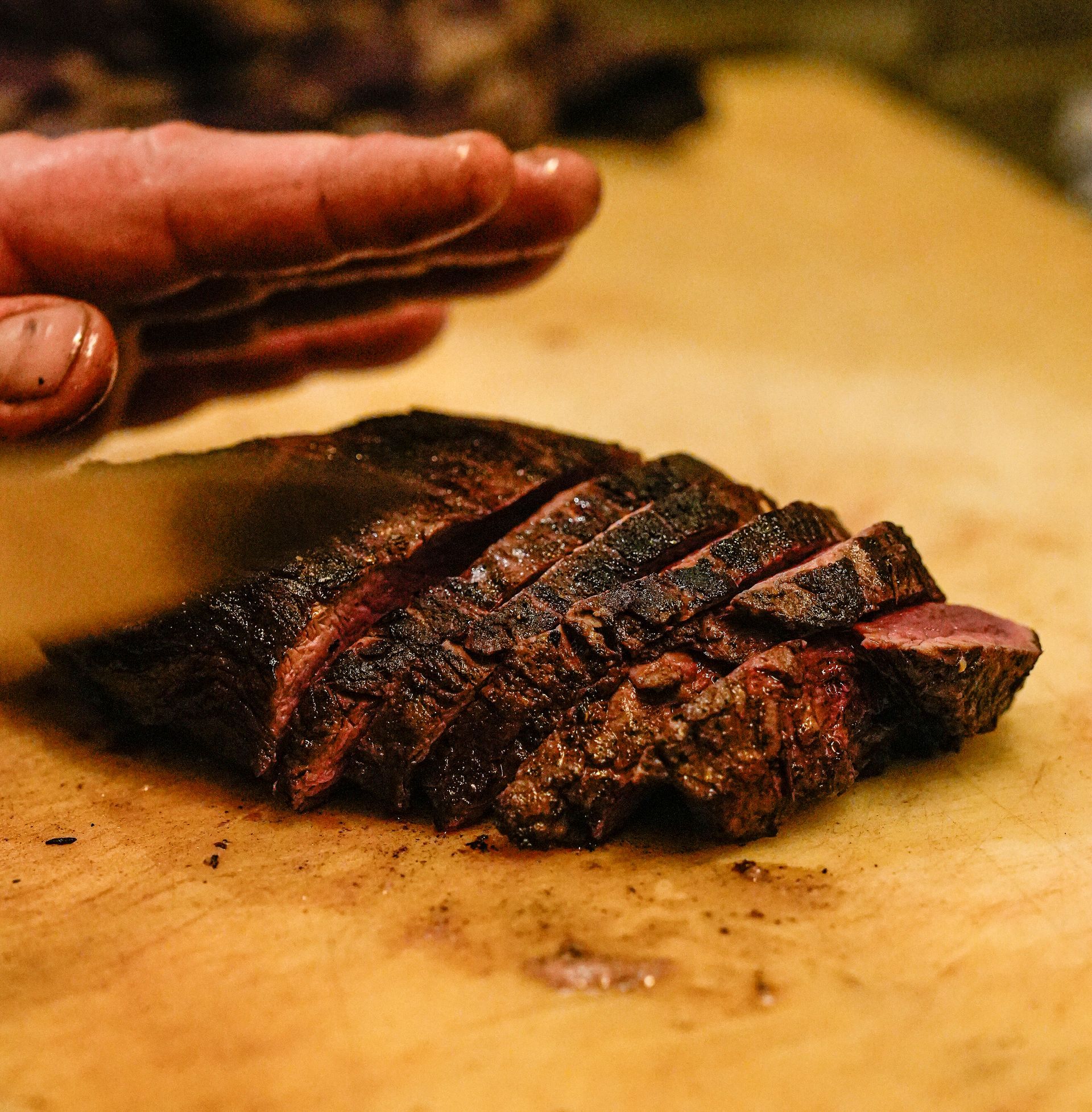 Iemand snijdt een stuk vlees op een snijplank. Bij Linke Loetje