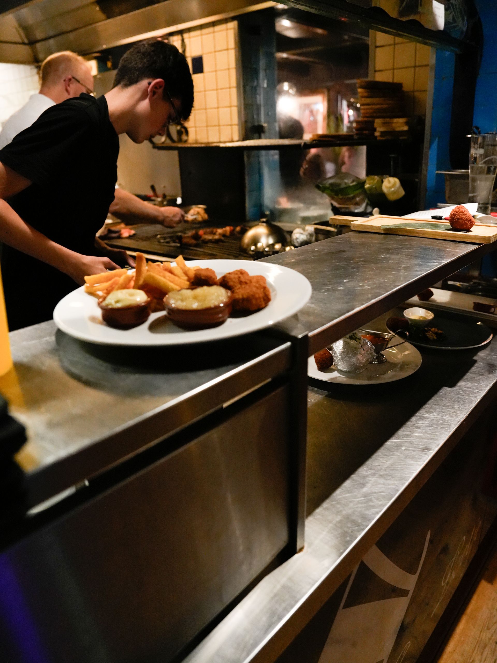 Een man bereidt eten in de keuken van een restaurant. Bij Linke Loetje