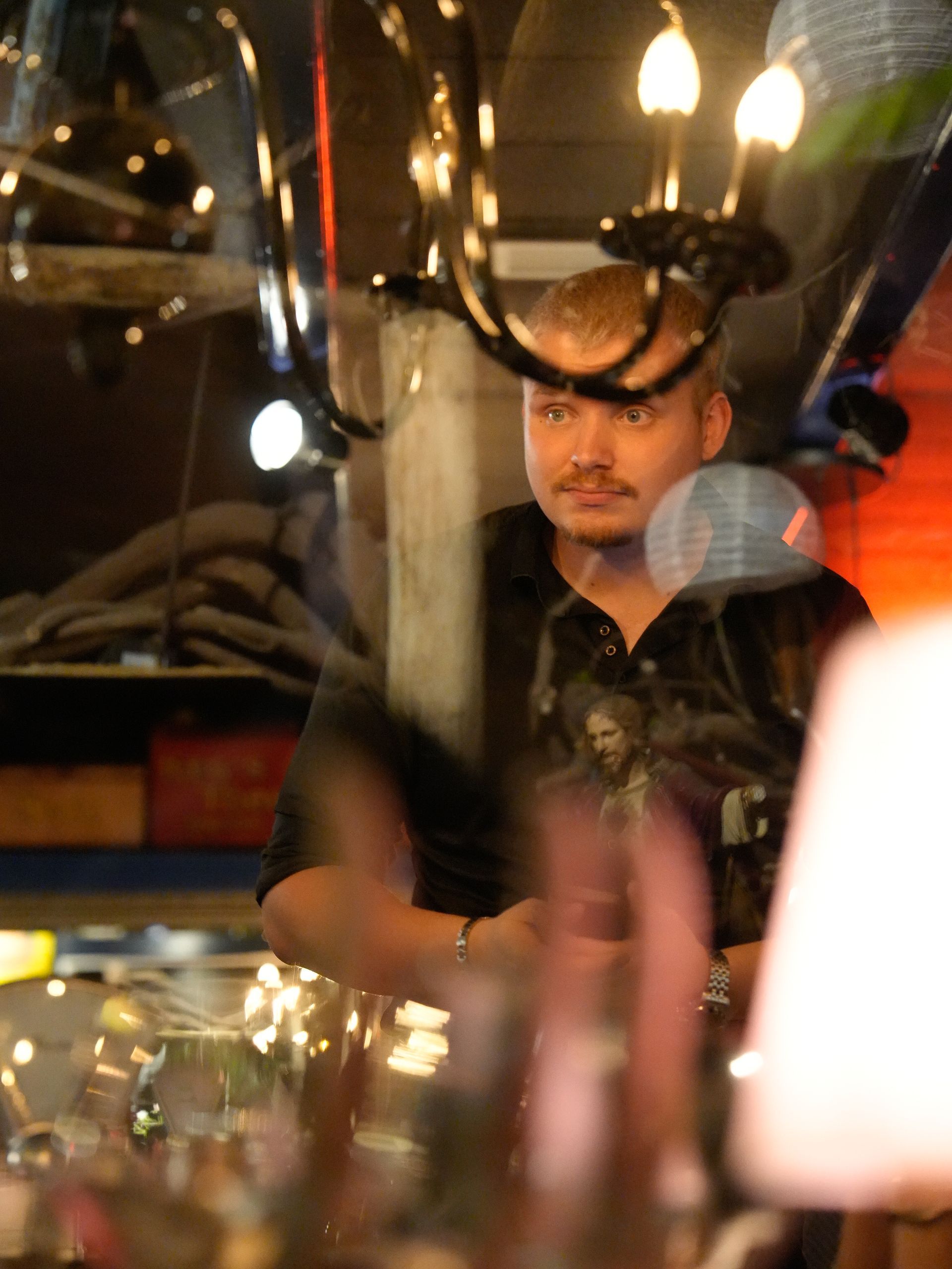 Een man in een zwart shirt staat voor een kroonluchter. Bij Linke Loetje