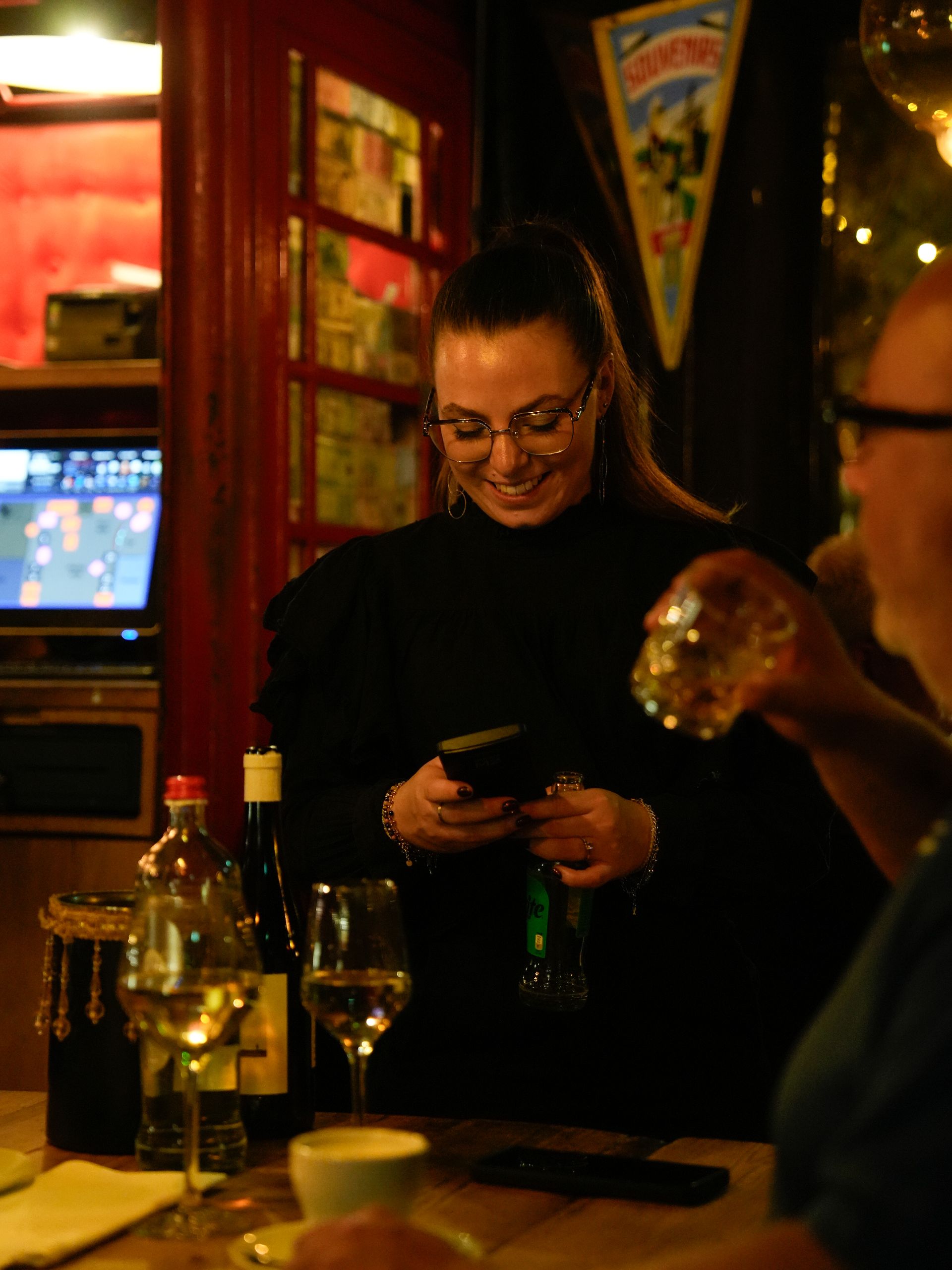 Een vrouw zit aan een tafel in een restaurant en kijkt op haar telefoon.. Bij Linke Loetje