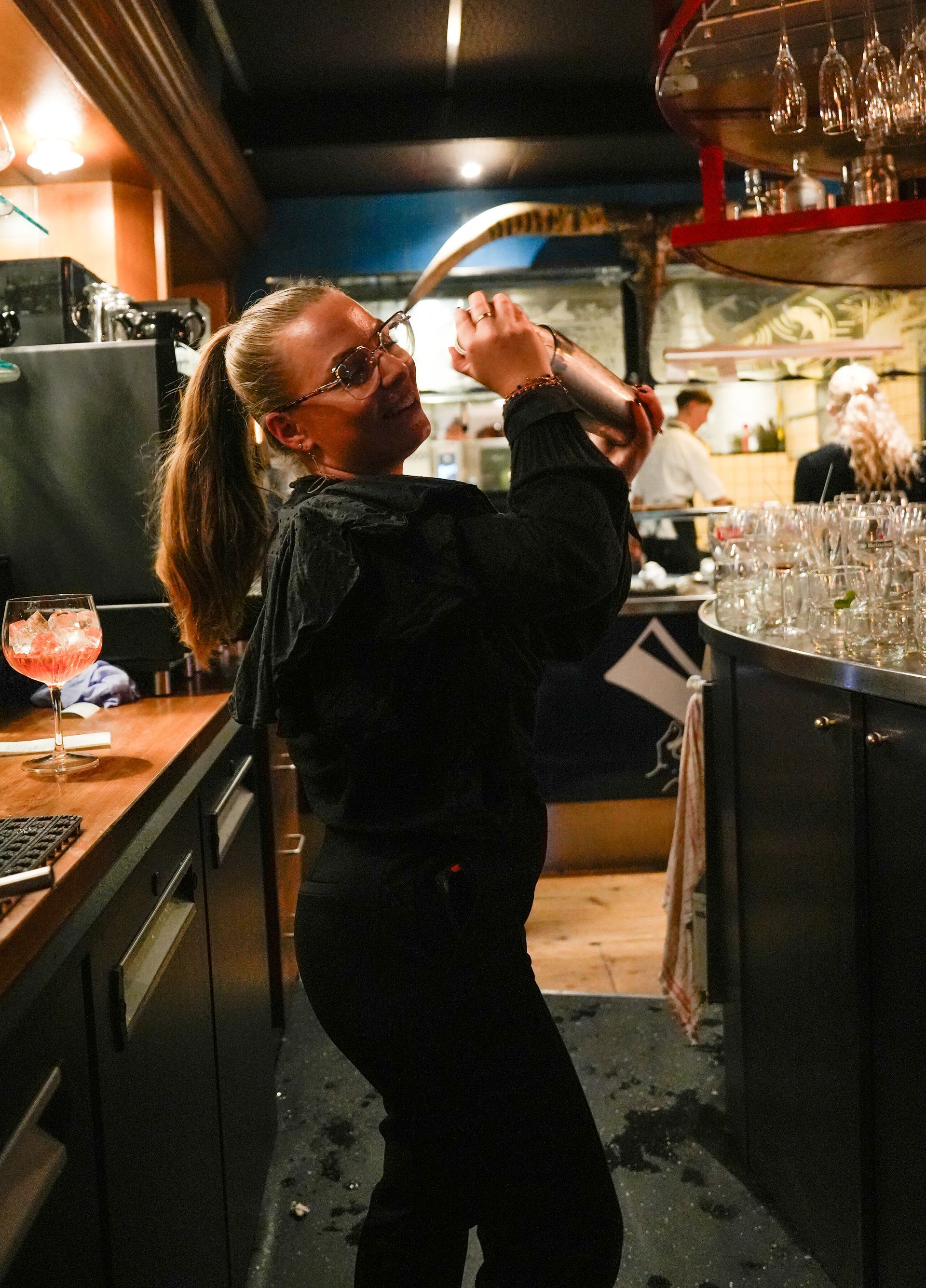 Een vrouw schudt een drankje in een bar. Bij Linke Loetje. Bij Linke Loetje