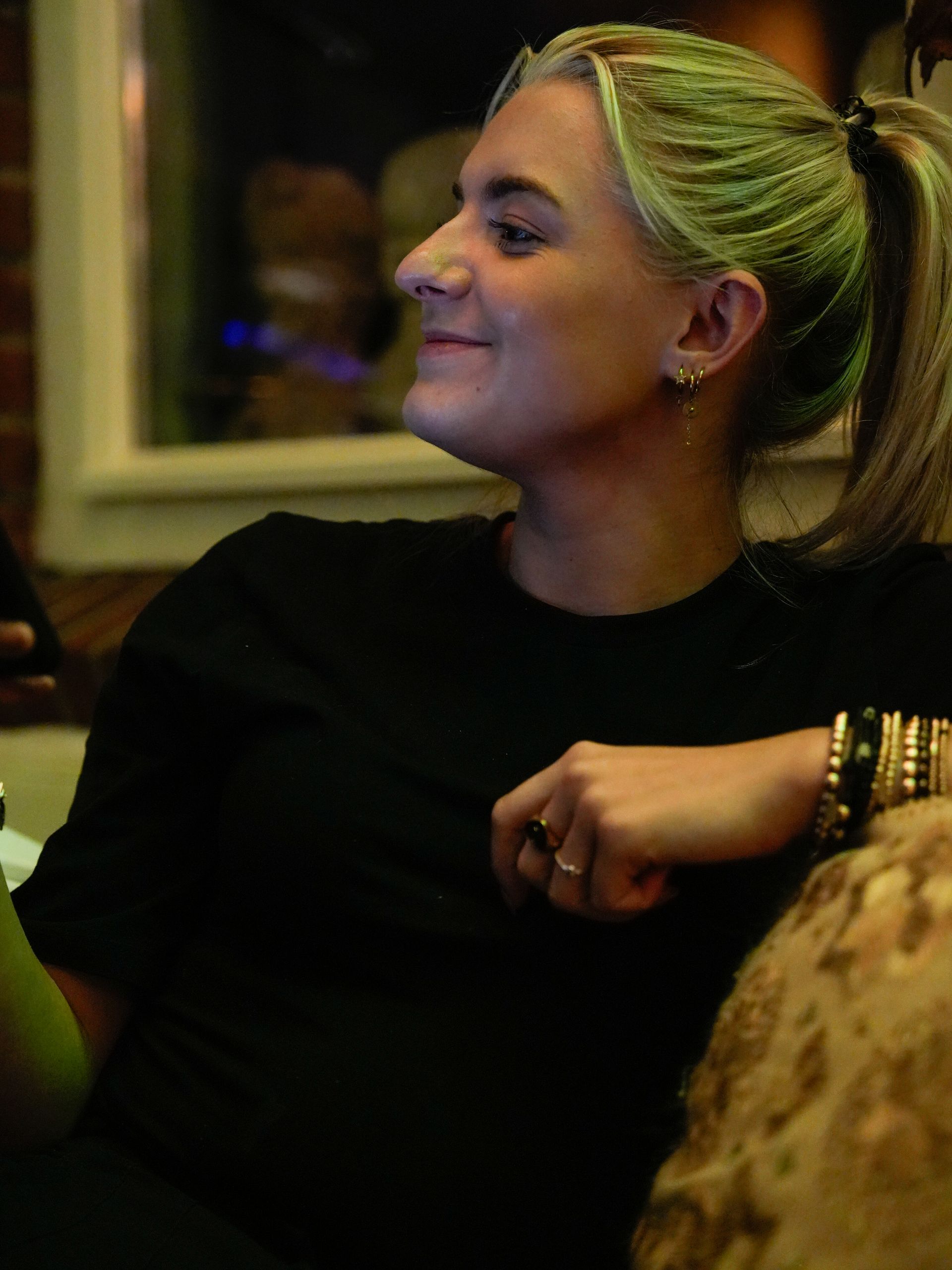 Een vrouw met groen haar zit op een bank en lacht. . Bij Linke Loetje. Bij Linke Loetje