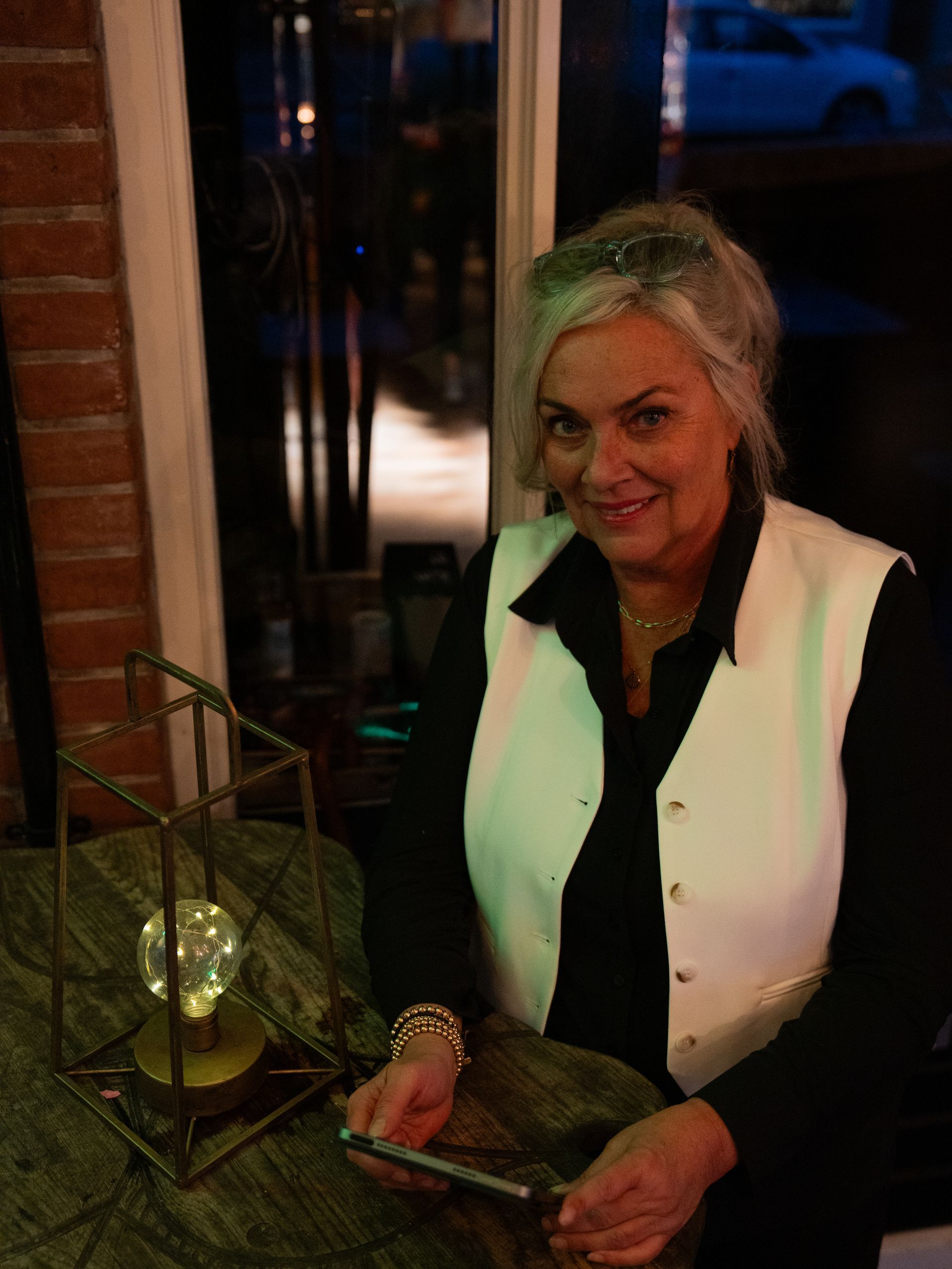 Een vrouw in een wit vest zit aan een tafel Bij Linke Loetje