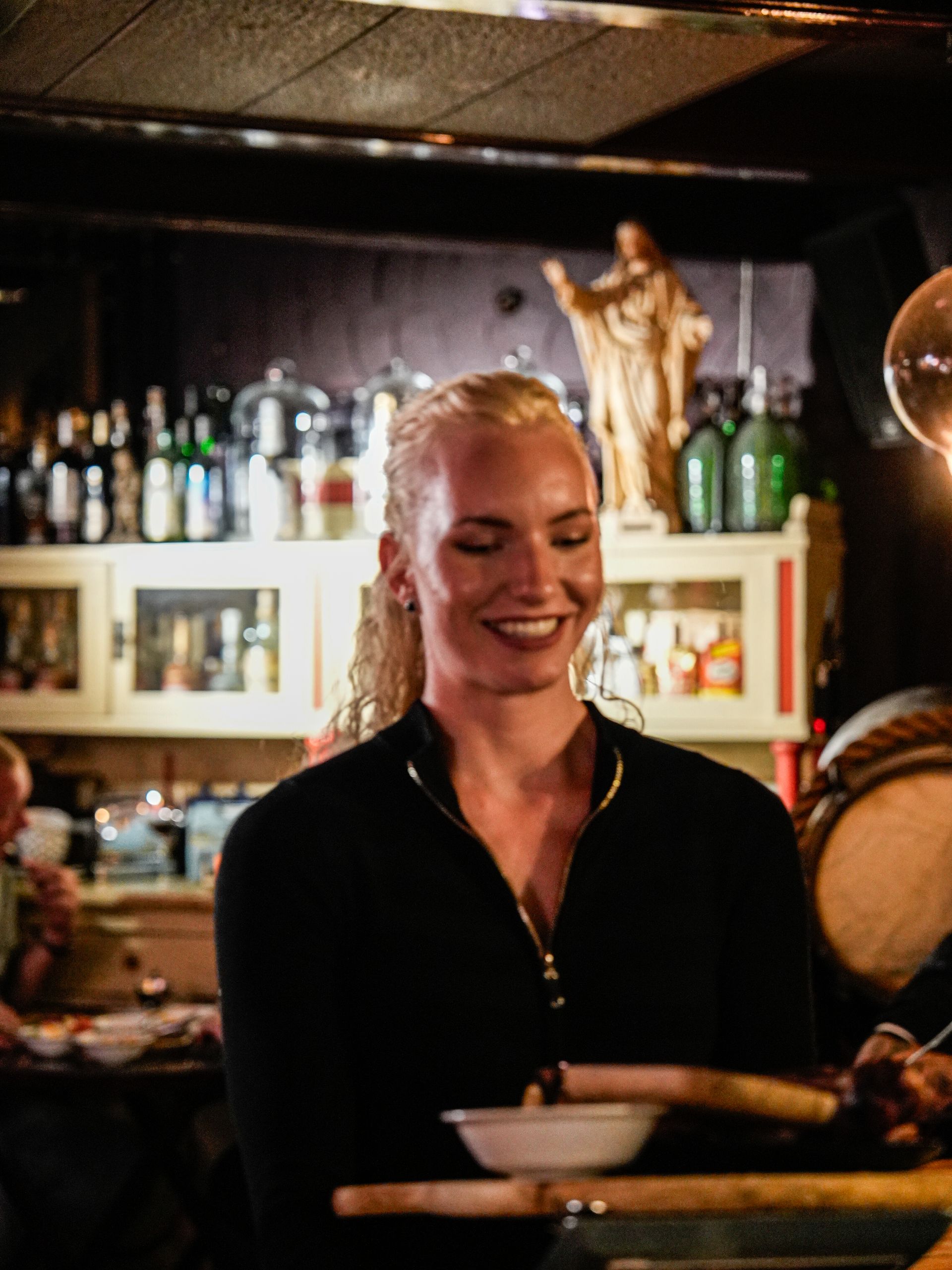 Een vrouw glimlacht terwijl ze een kom vasthoudt in een restaurant.. Bij Linke Loetje