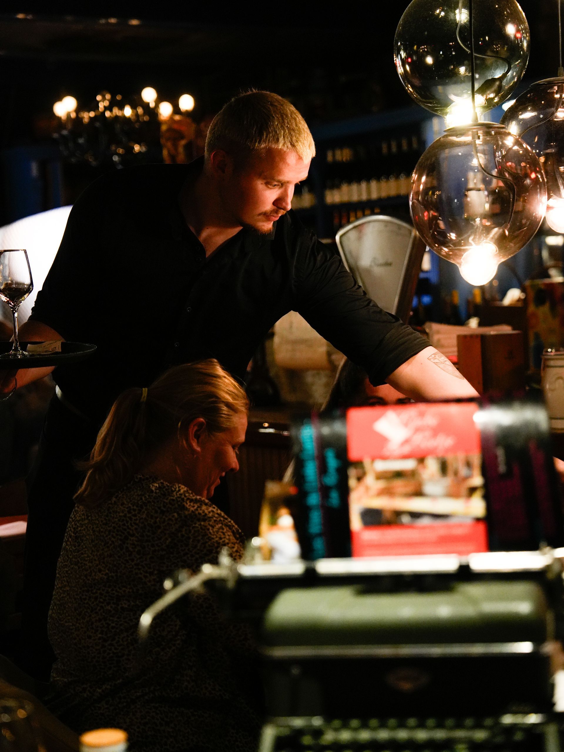 Een man en een vrouw zitten aan een tafel voor een typemachine. Bij Linke Loetje