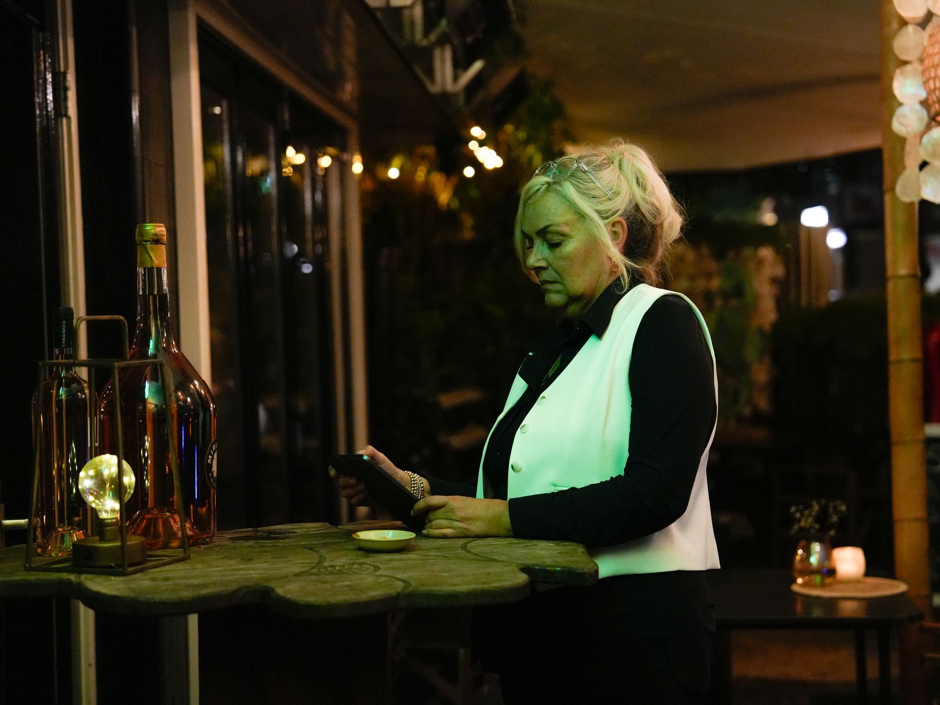 Een vrouw zit aan een tafel en kijkt naar haar telefoon.. Bij Linke Loetje 