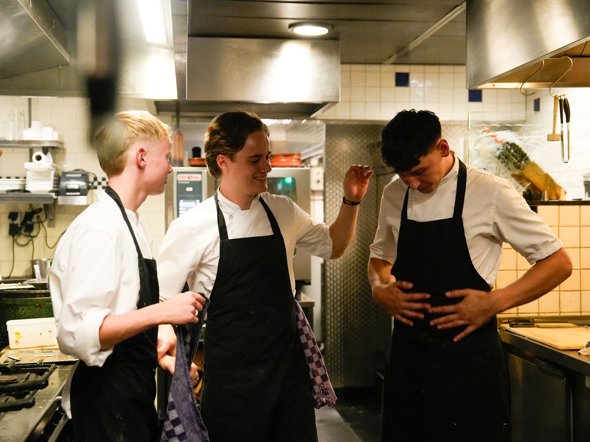 Drie mannen met schorten staan ​​in een keuken met elkaar te praten.. Bij Linke Loetje