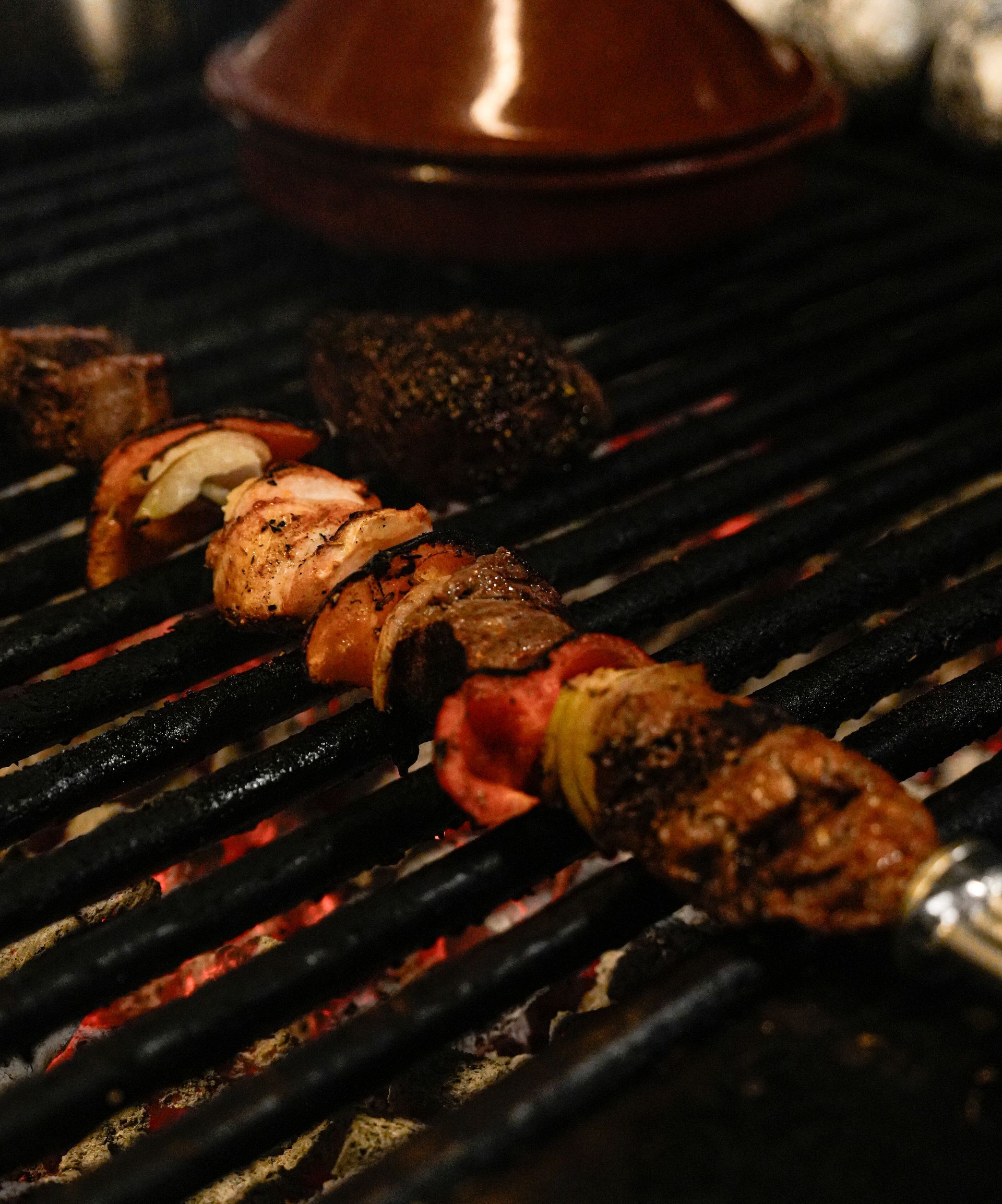 Spiesjes vlees worden gekookt op een grill met een pot op de achtergrond. Bij Linke Loetje
