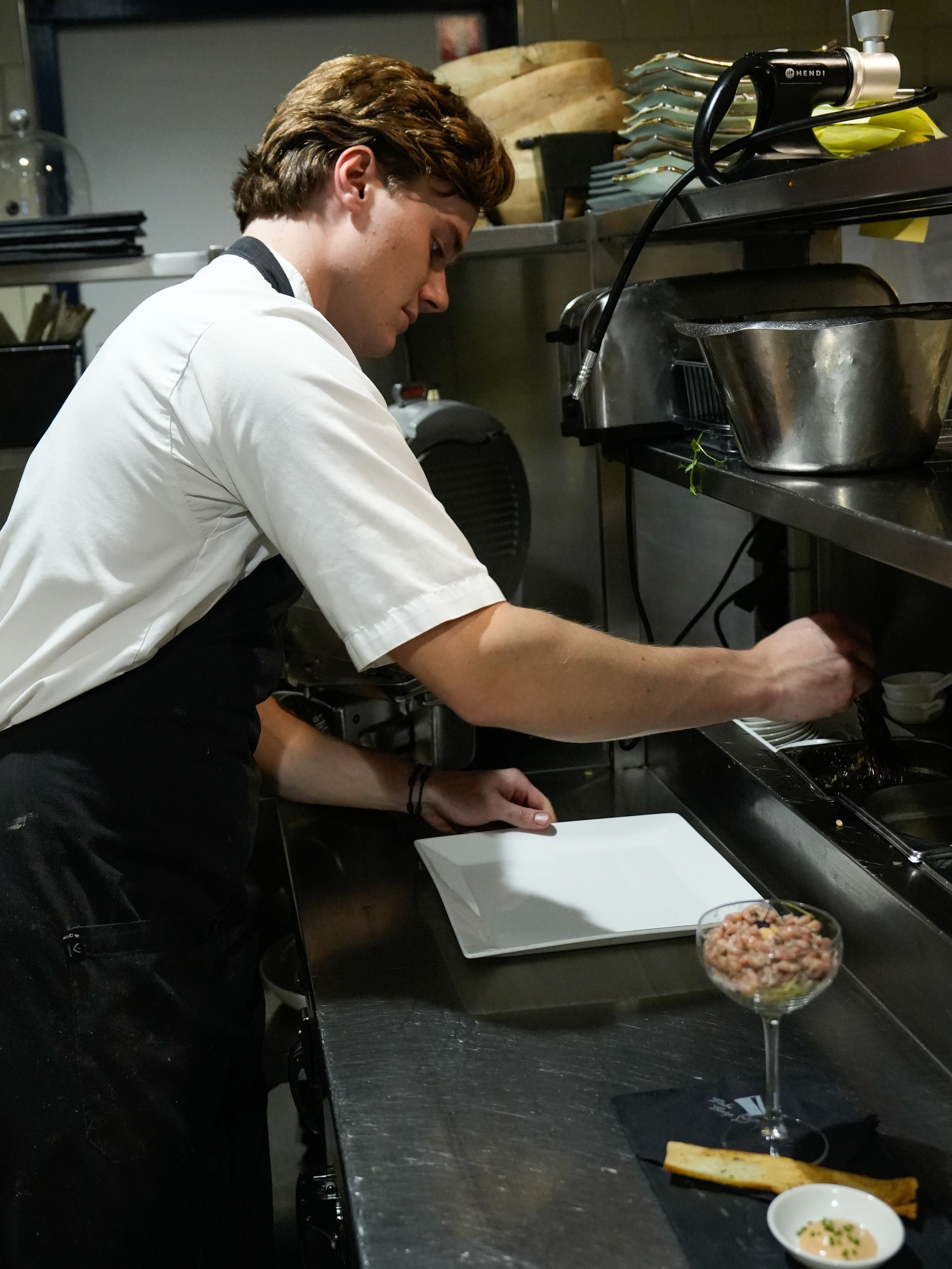 Een man met een schort bereidt eten in een keuken. Bij Linke Loetje
