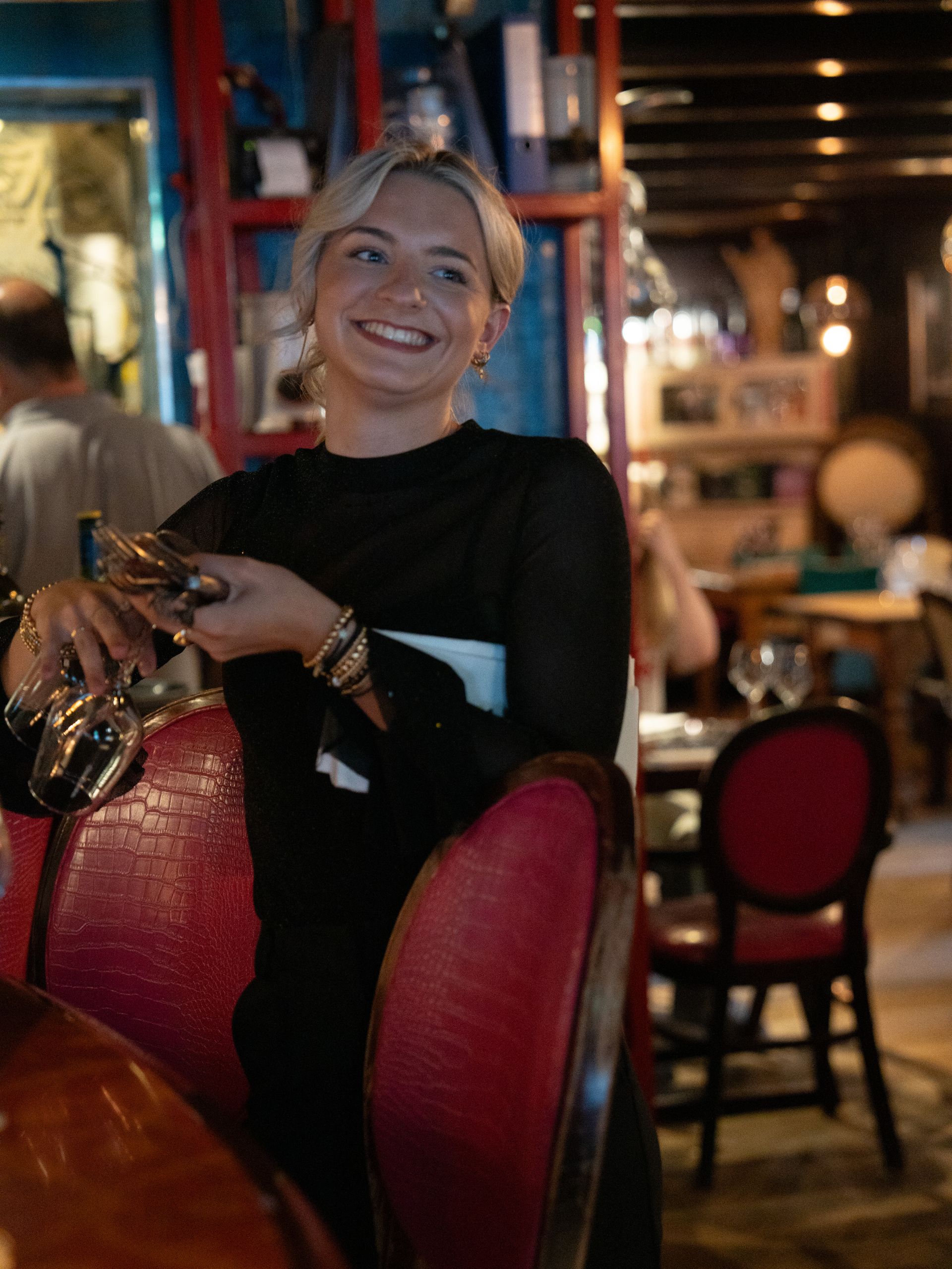 Een vrouw zit aan een tafel in een restaurant met een glas wijn in haar hand.. Bij Linke Loetje