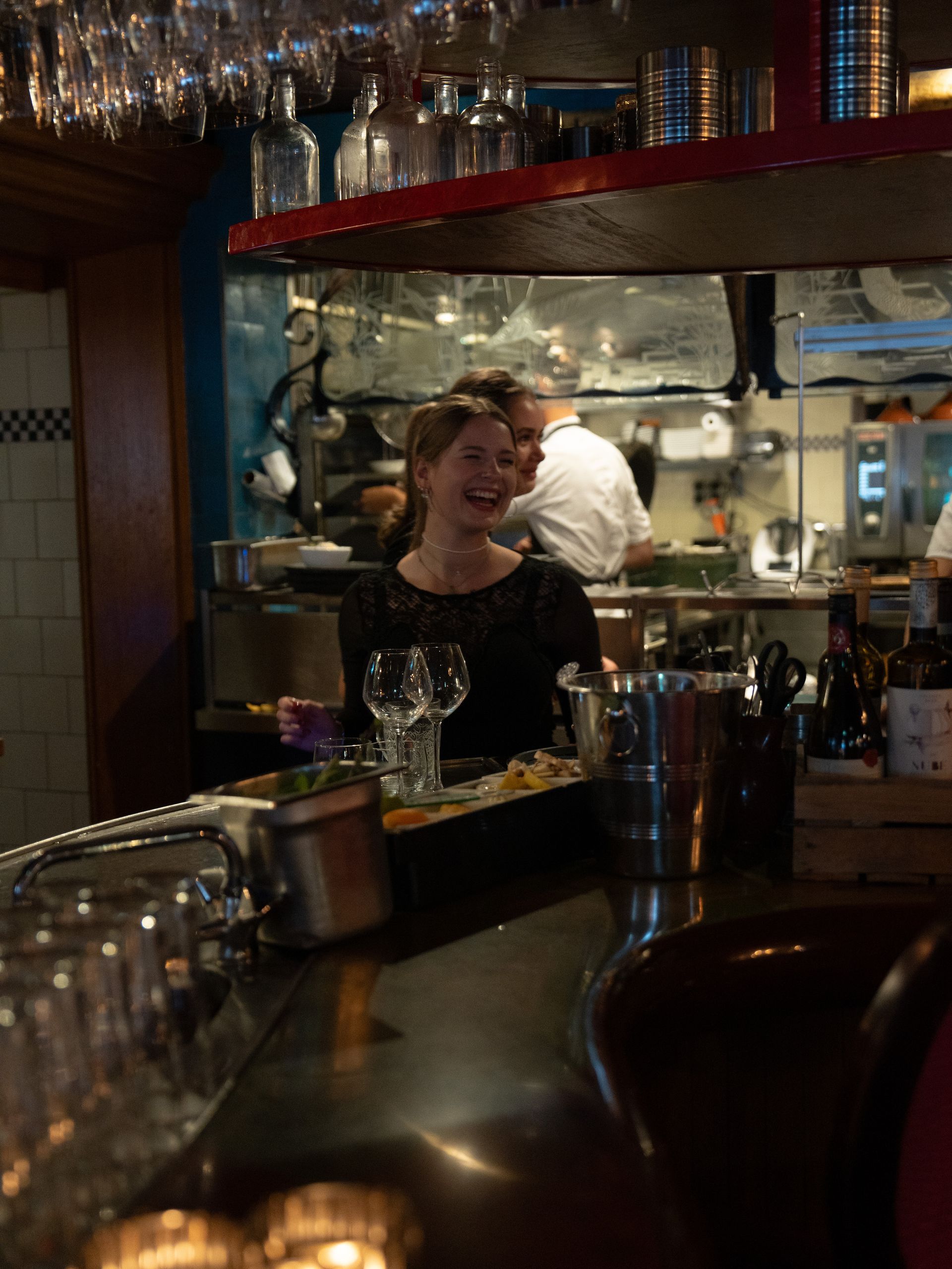 Een vrouw zit lachend aan de balie in een restaurant. Bij Linke Loetje