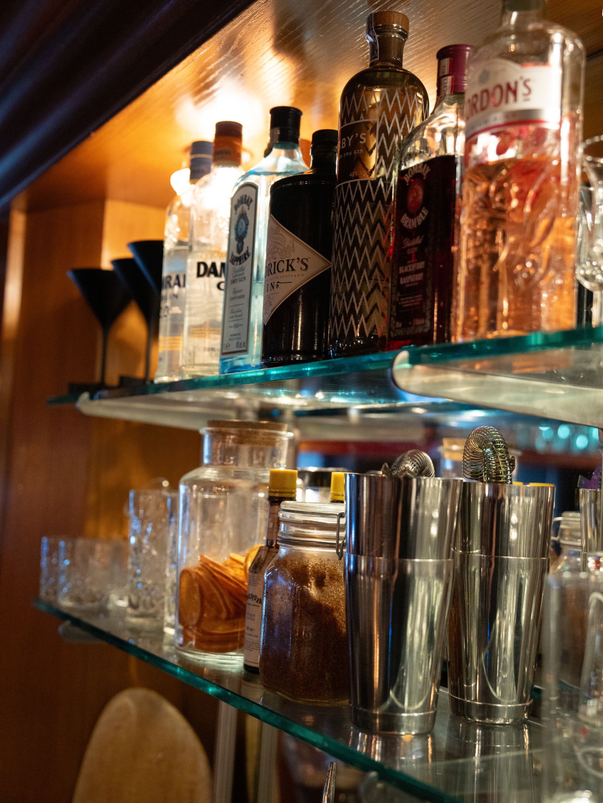 Een glazen plank gevuld met flessen en glazen, waaronder een fles eddon's gin. Bij Linke Loetje