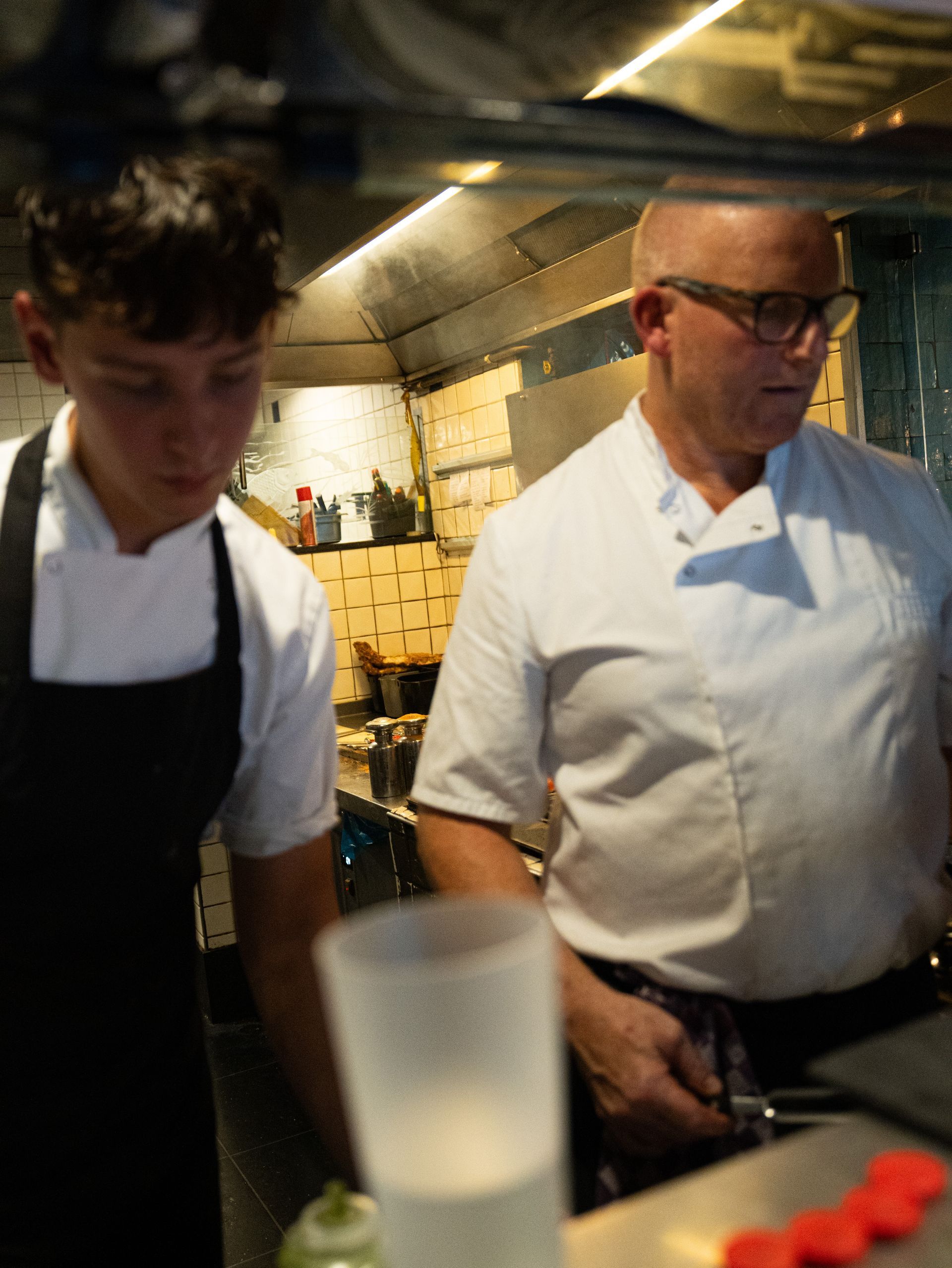 Twee koks werken in een keuken met een glas water op de voorgrond