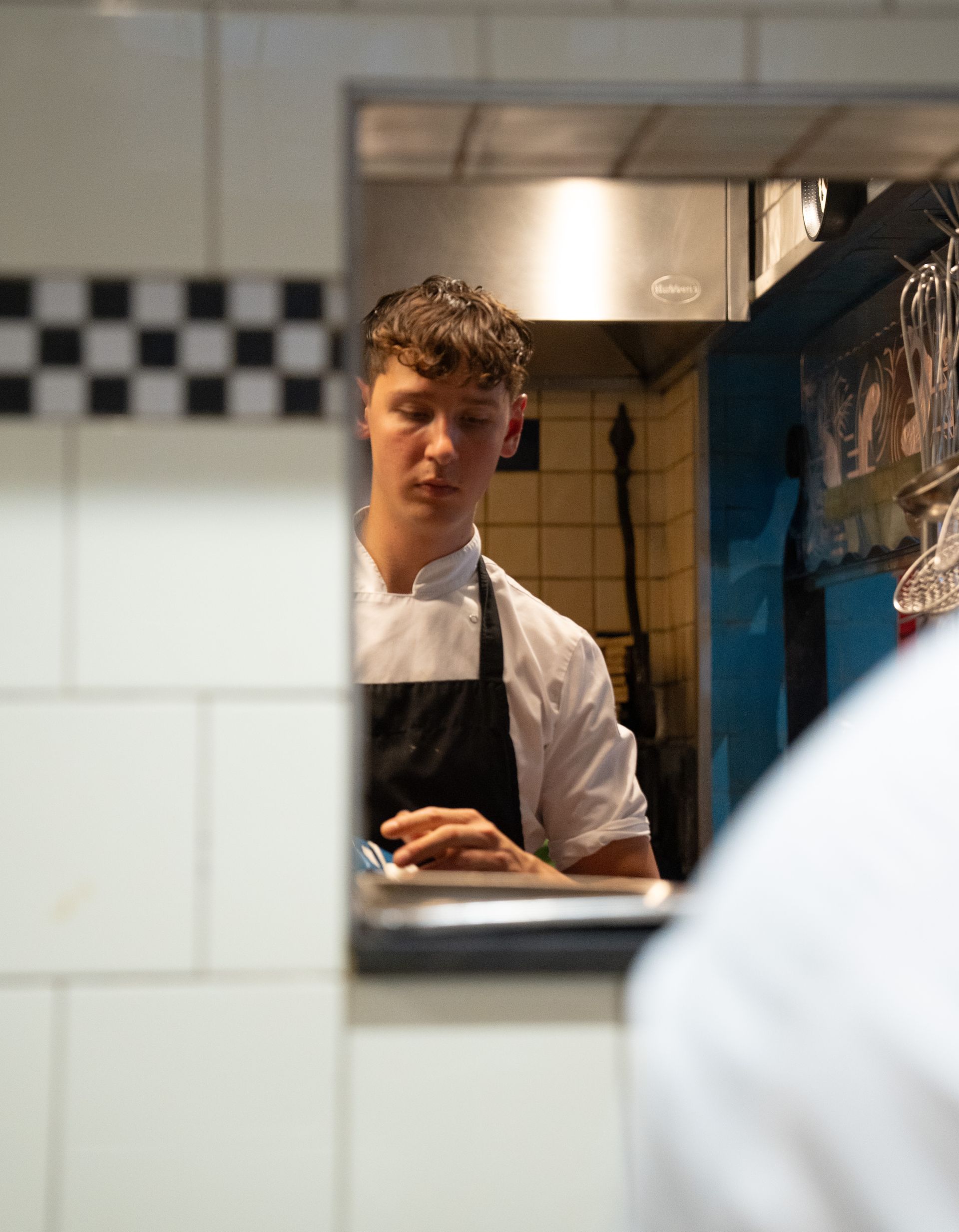 Een man met een schort kijkt door een raam in een keuken. . Bij Linke Loetje
