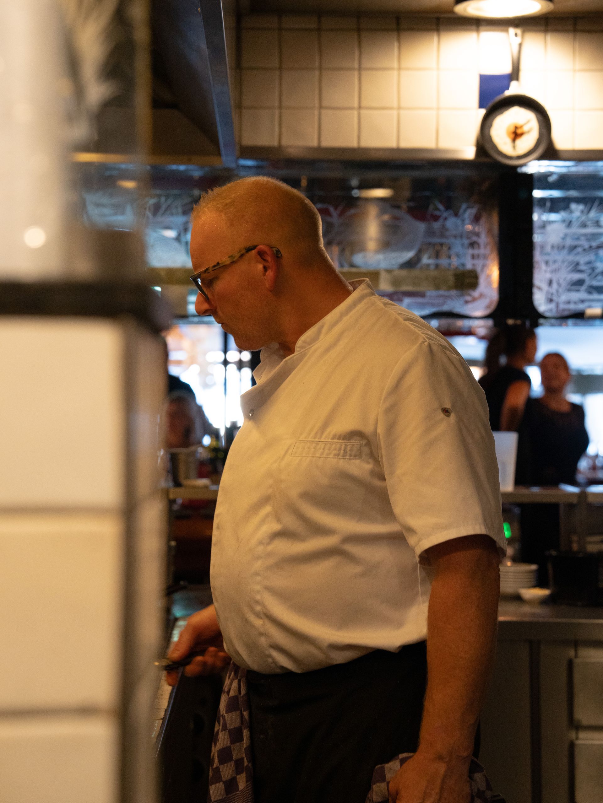 Een man in een wit overhemd staat in de keuken.. Bij Linke Loetje