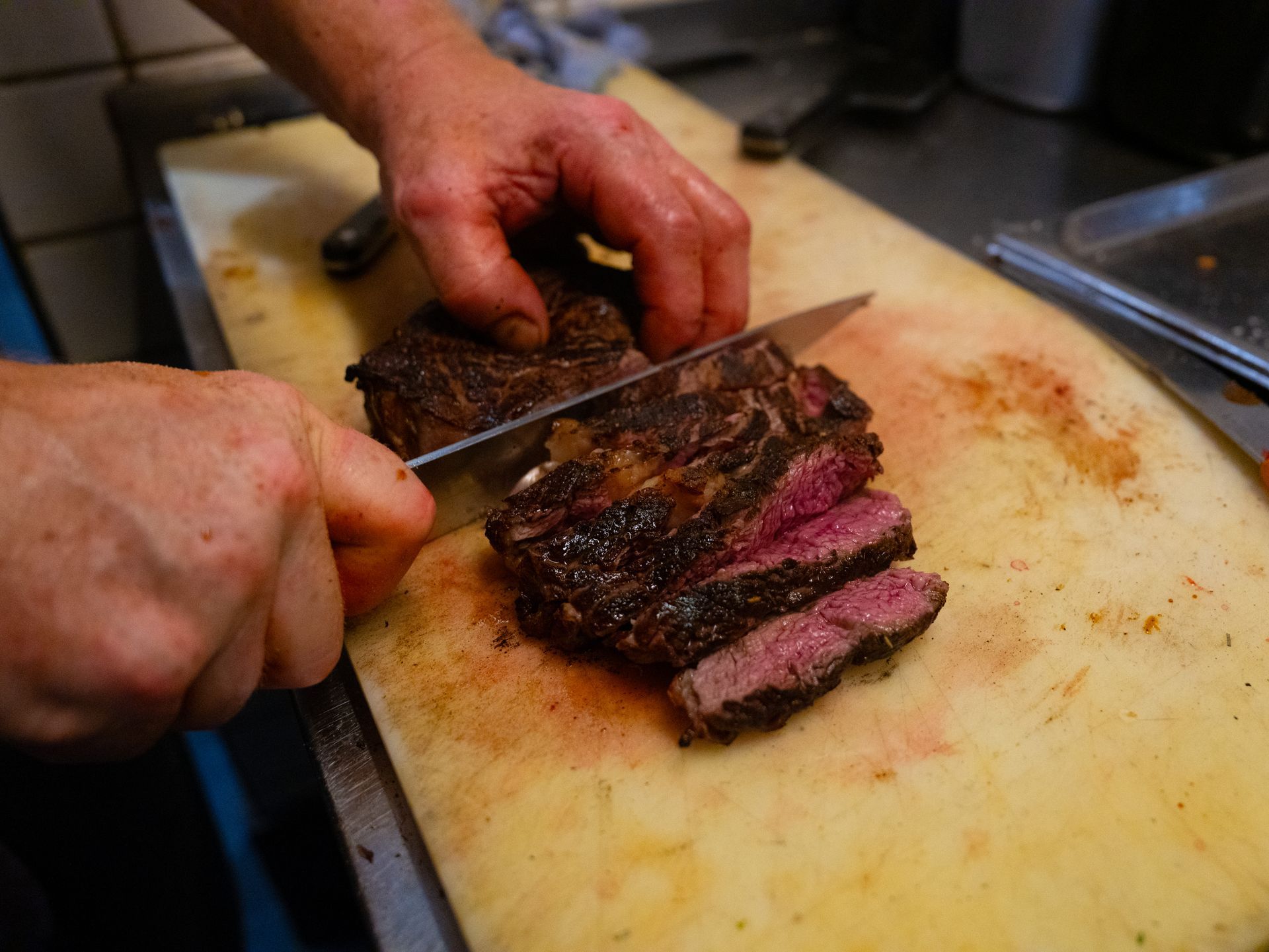 Iemand snijdt een stuk vlees op een snijplank.. Bij Linke Loetje