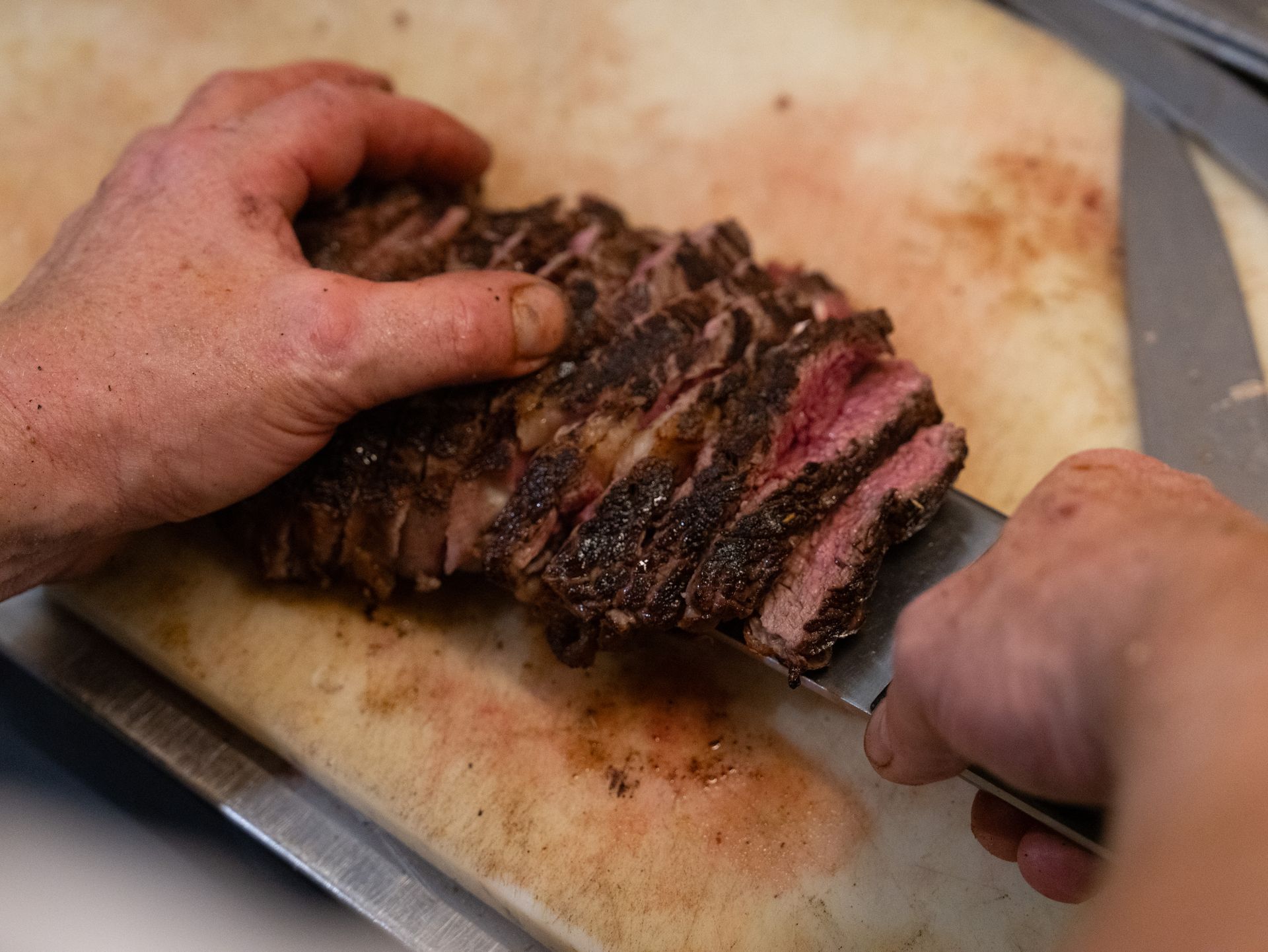 Iemand snijdt een stuk vlees op een snijplank.. Bij Linke Loetje