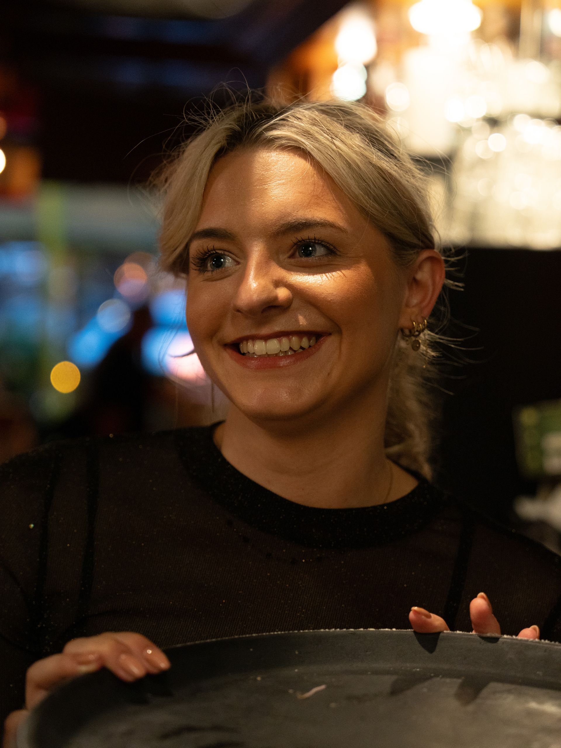 Een vrouw lacht terwijl ze een dienblad vasthoudt in een restaurant.  bij Linke Loetje