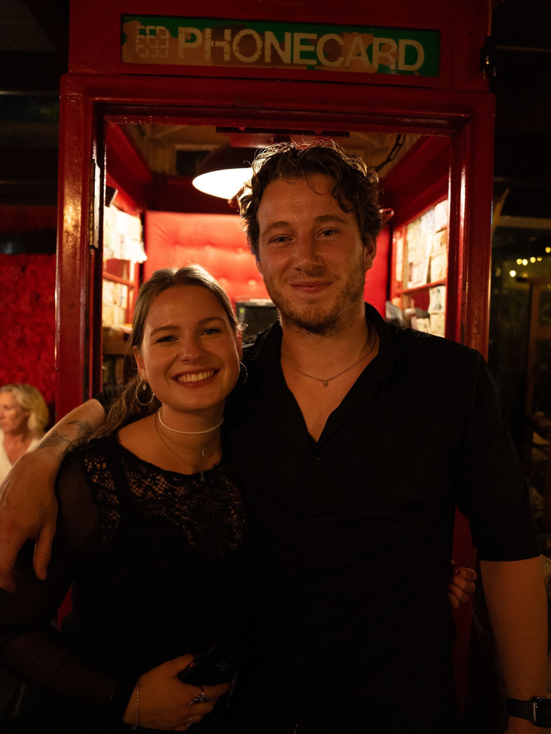 Een man en een vrouw poseren voor een foto voor een telefooncel.. Bij Linke Loetje