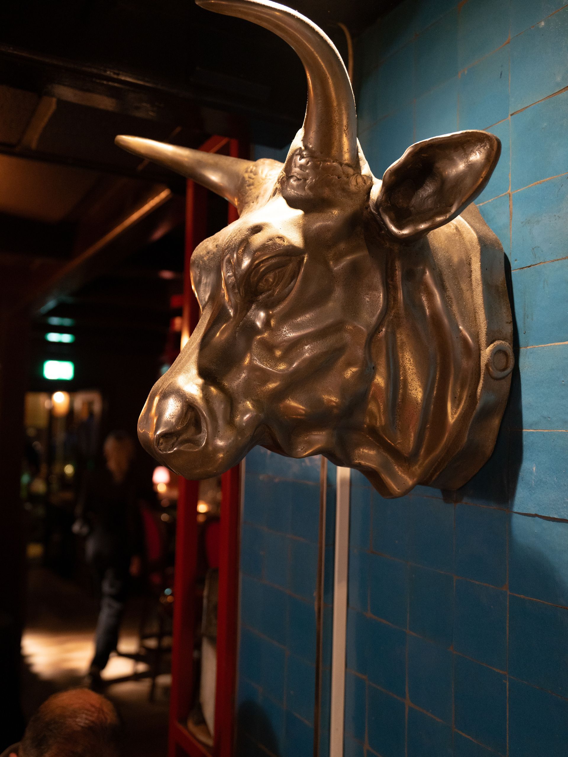 Een standbeeld van een stierenkop hangt aan een blauwe muur. Bij Linke Loetje