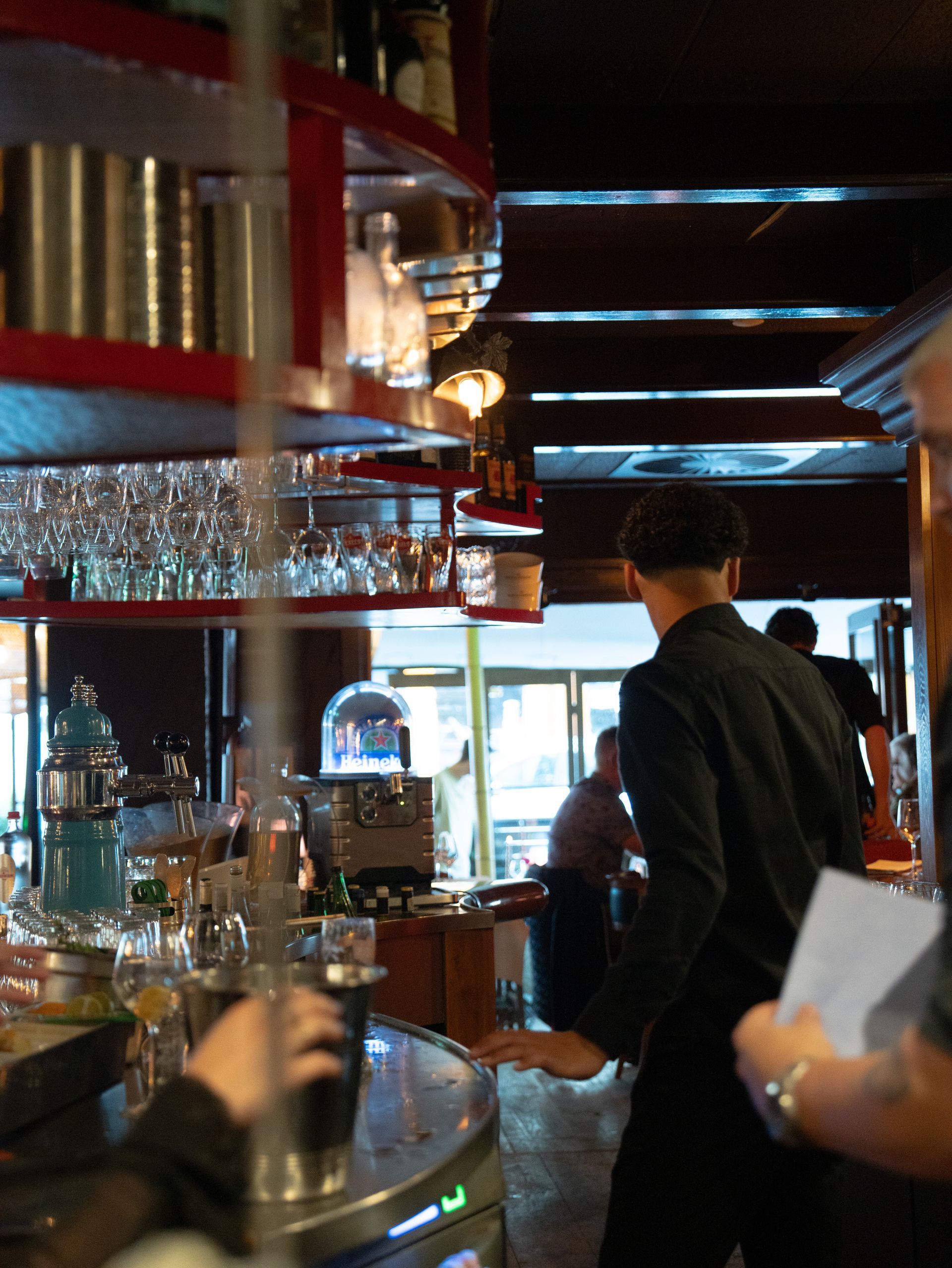 Een man in een zwart pak staat in een bar. Bij Linke Loetje