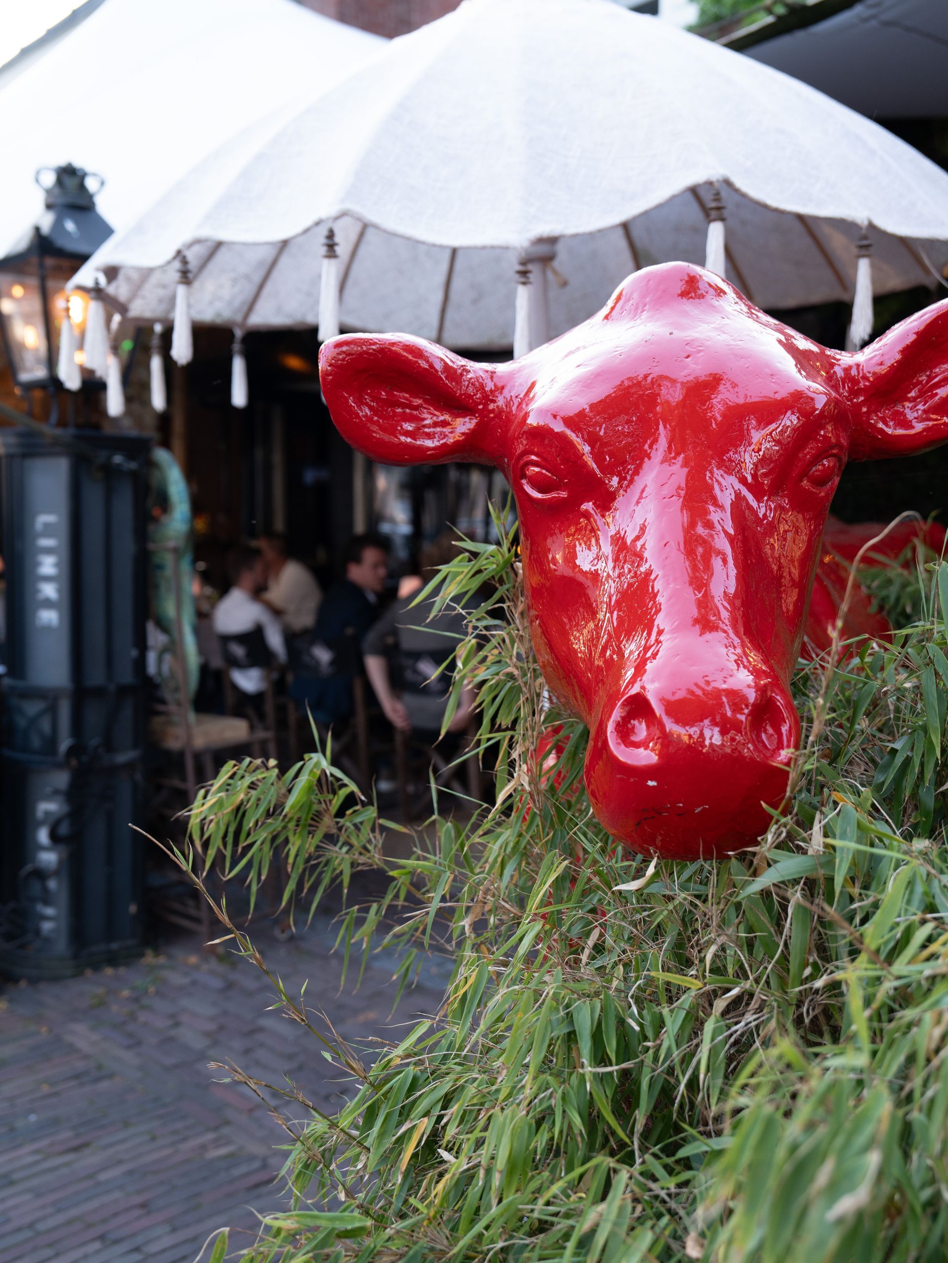 Een standbeeld van een rode koe staat voor een restaurant. Bij Linke Loetje