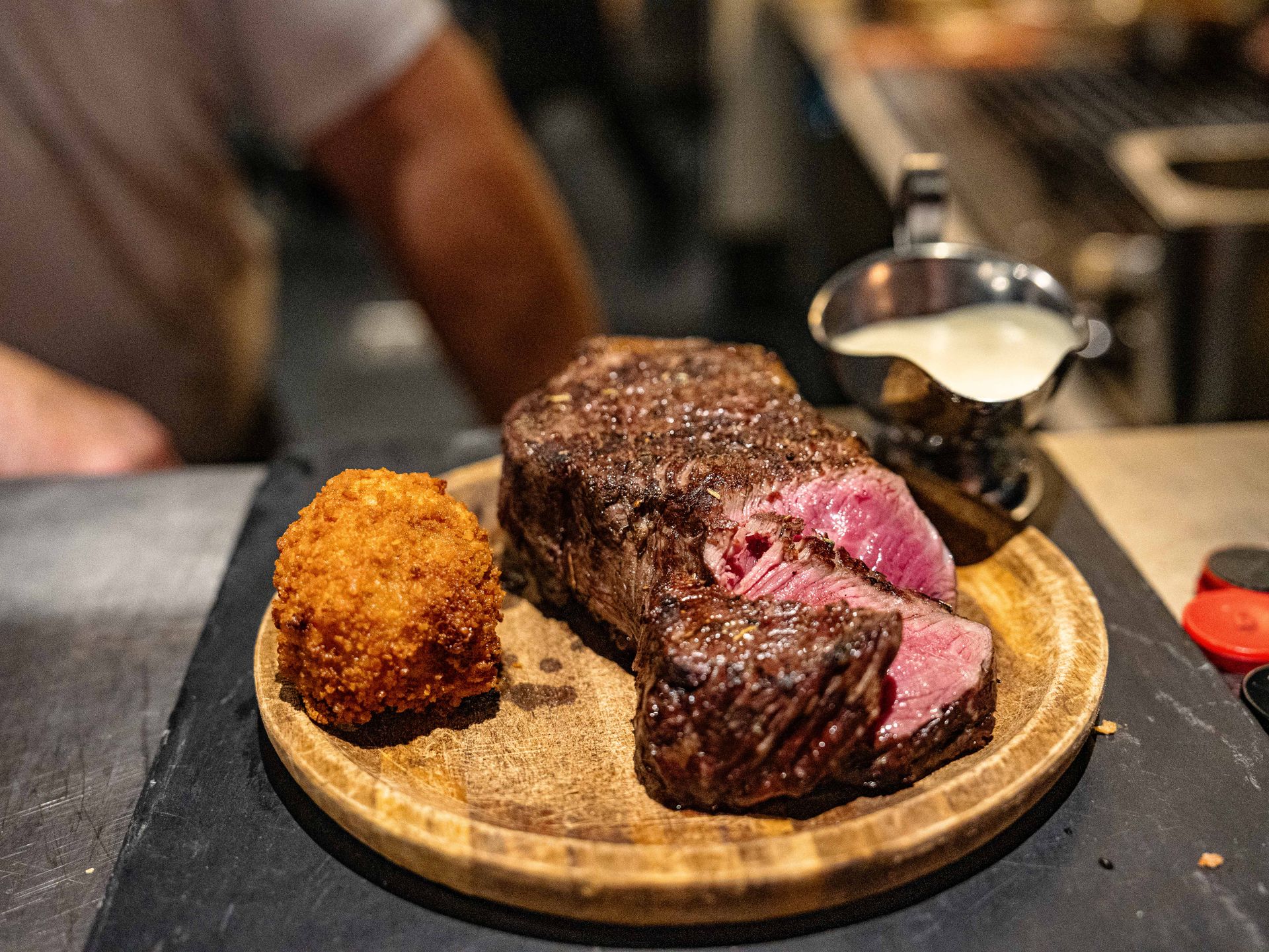 Een stuk biefstuk en een stuk gefrituurd voedsel op een houten bord bij Linke Loetje