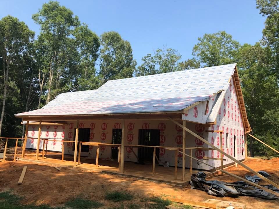 Construction of a house with a porch, surrounded by trees; red and white exterior.