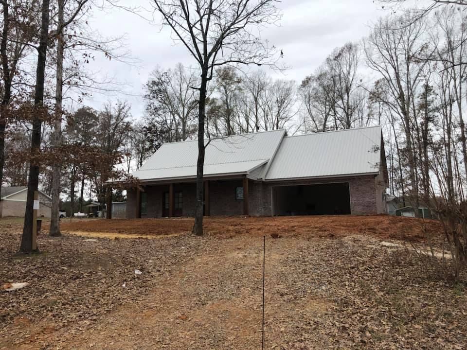 New house under construction with a white metal roof, on a wooded lot.