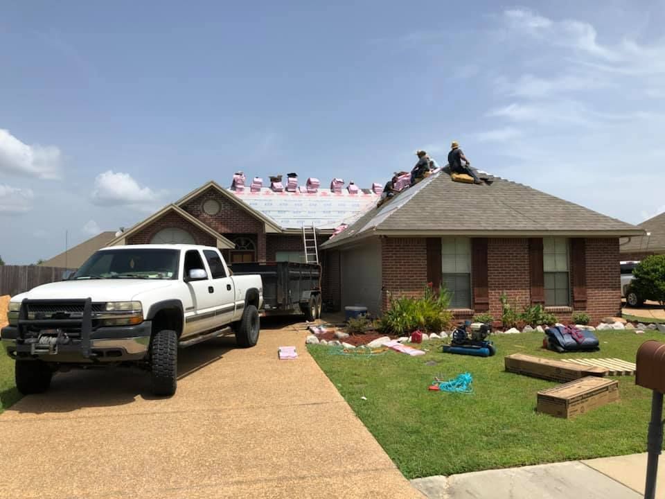 Roofers replacing a roof on a brick home. A truck and trailer are in the driveway.