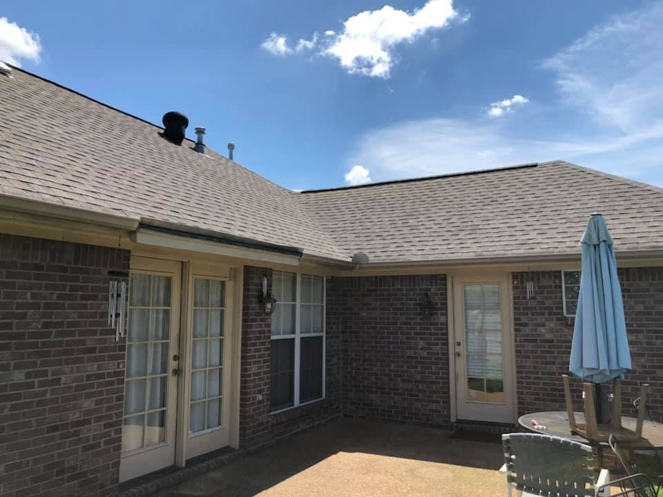 Brick house exterior with a brown roof, French doors, patio, and blue sky.