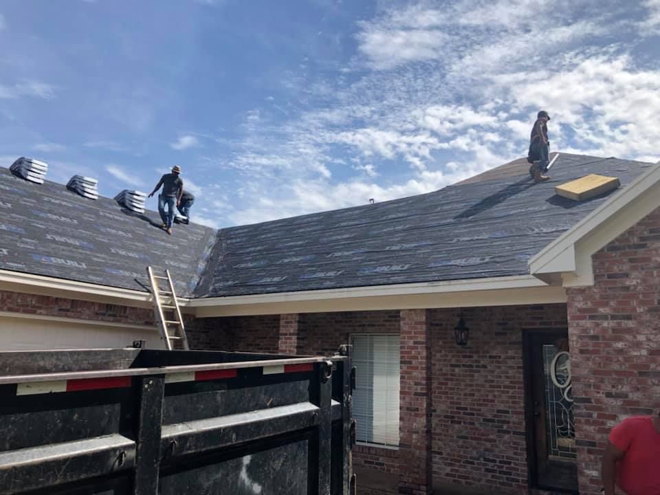 Roofers installing shingles on a brick house under a partly cloudy sky.