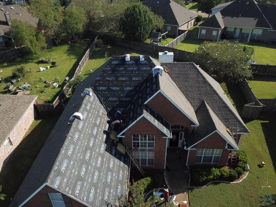 Aerial view of a house with a roof being replaced by workers. The roof is partially covered in new material.