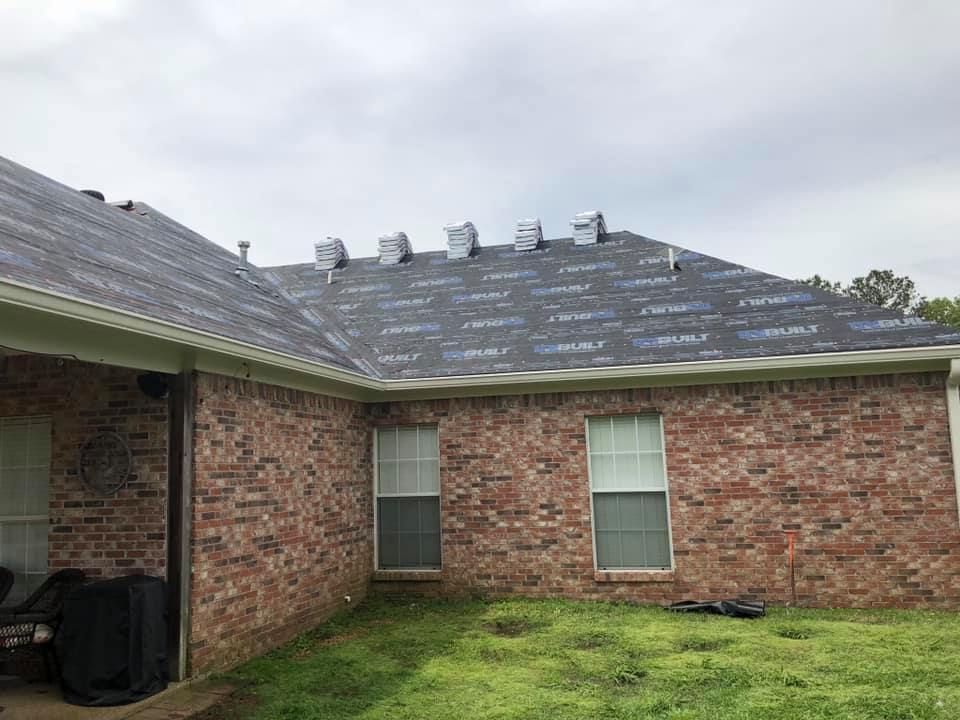 Brick house with new roofing material being installed; cloudy sky.