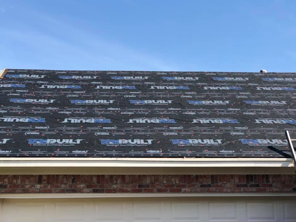 Roof underlayment with black and blue print on a residential house under a blue sky.