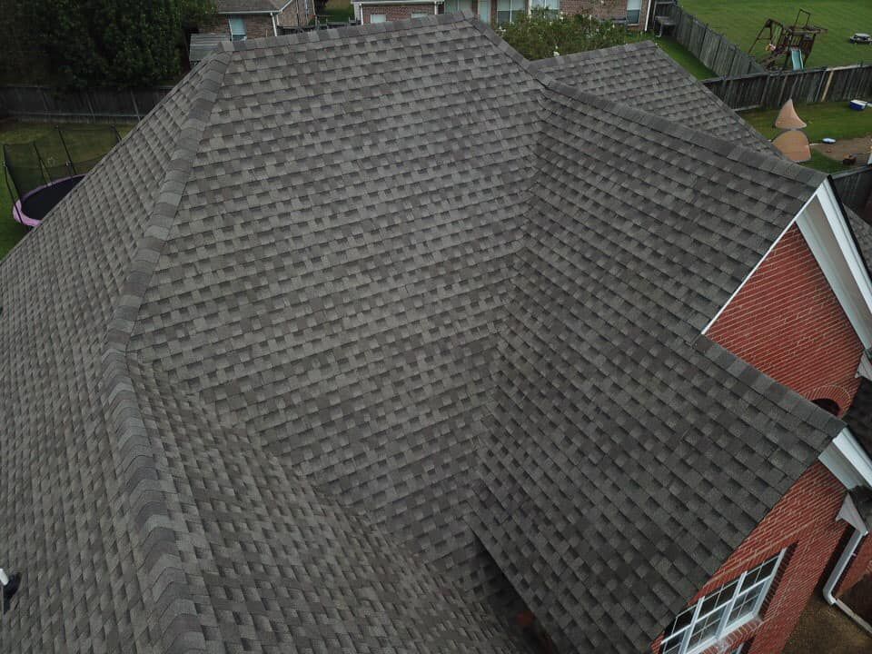 Overhead view of a house with a gray shingle roof. A brick facade and backyard visible.